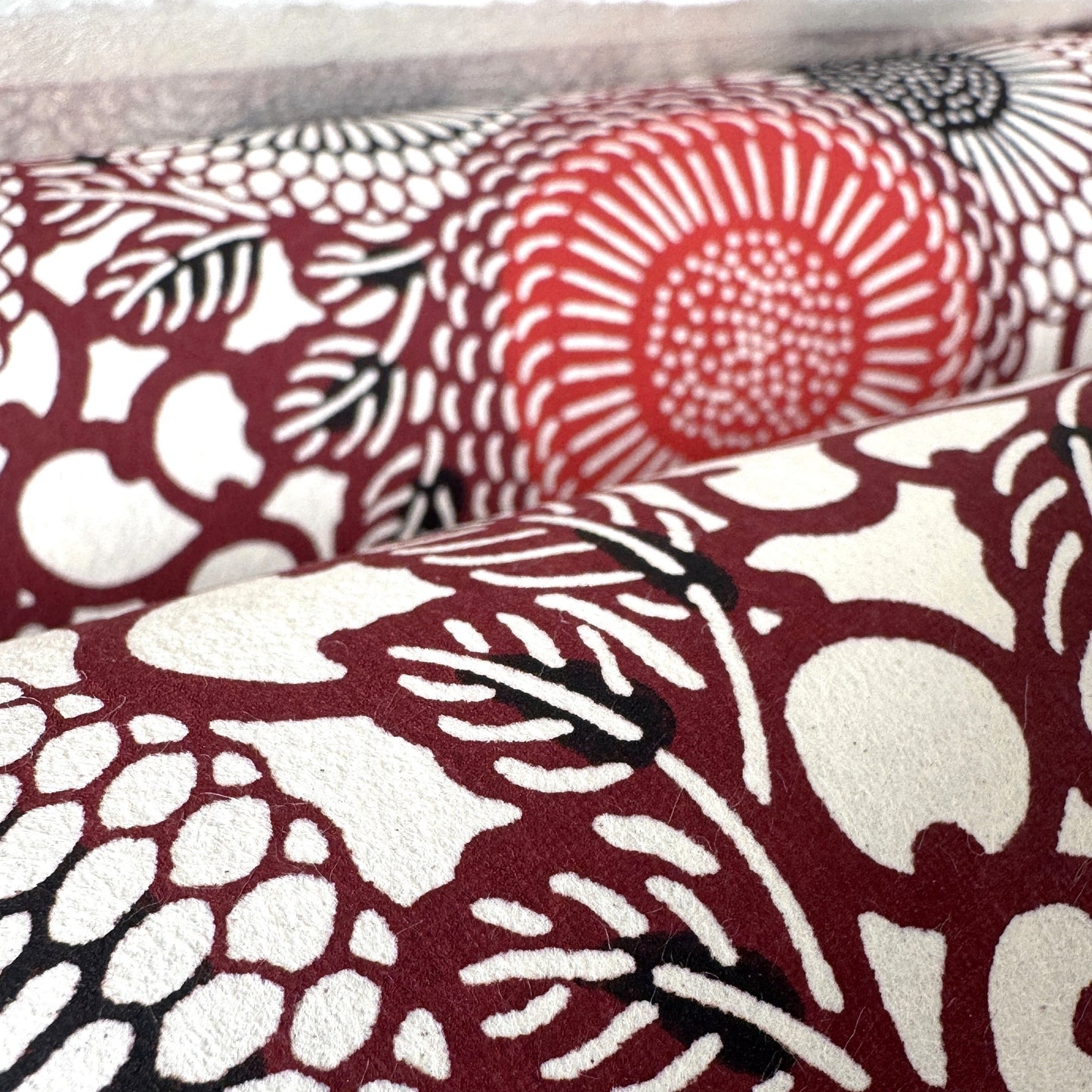 Japanese katazome-shi paper stencil-dyed with a pattern of stylised kiko flowers in red, maroon and black on an ivory paper. Close-up