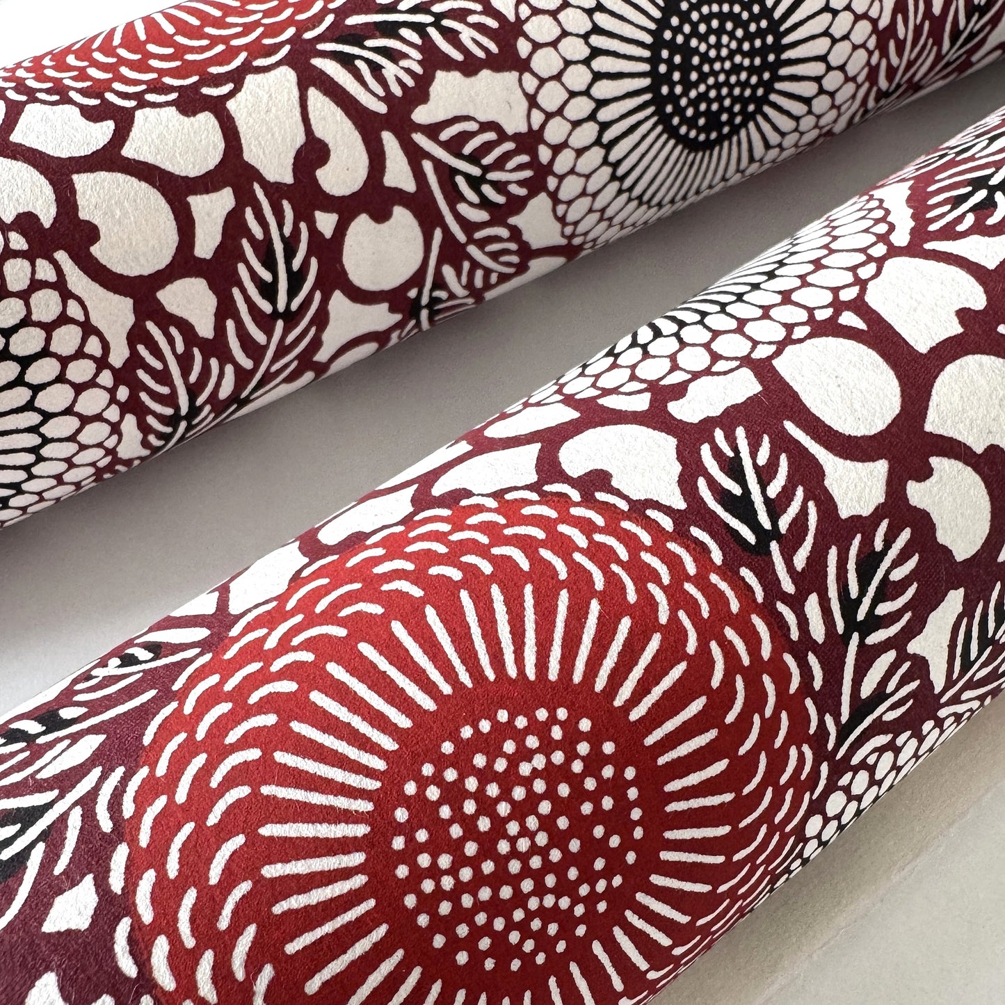Japanese katazome-shi paper stencil-dyed with a pattern of stylised kiko flowers in red, maroon and black on an ivory paper. Close up of the red flower