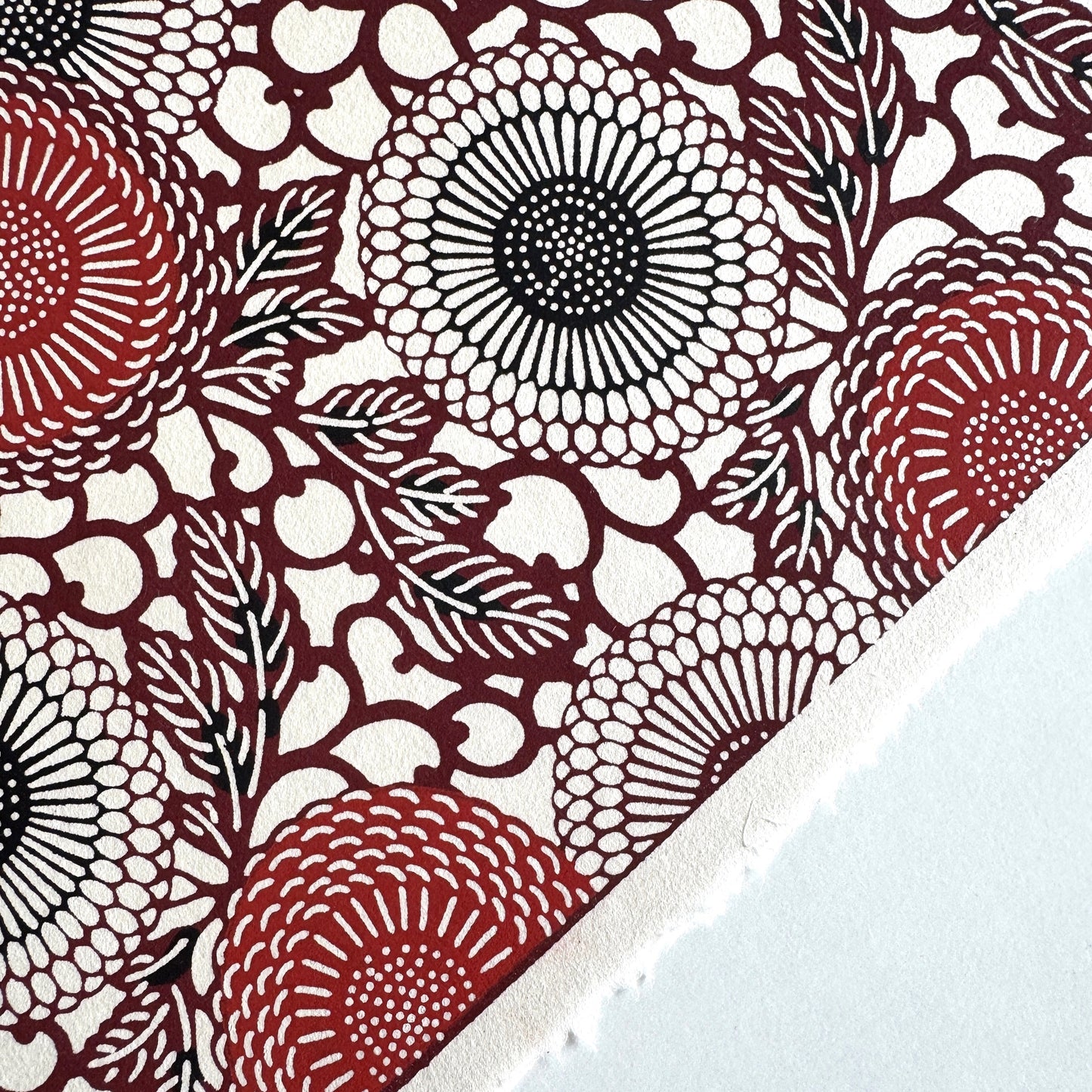 Japanese katazome-shi paper stencil-dyed with a pattern of stylised kiko flowers in red, maroon and black on an ivory paper.