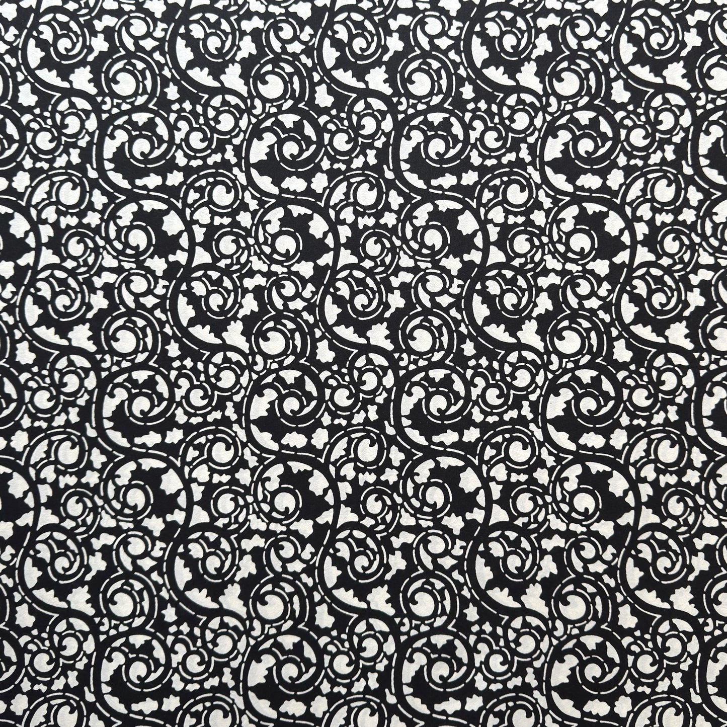 Japanese katazome-shi paper with bold black arabesque vines (karakusa) pattern on an ivory paper.