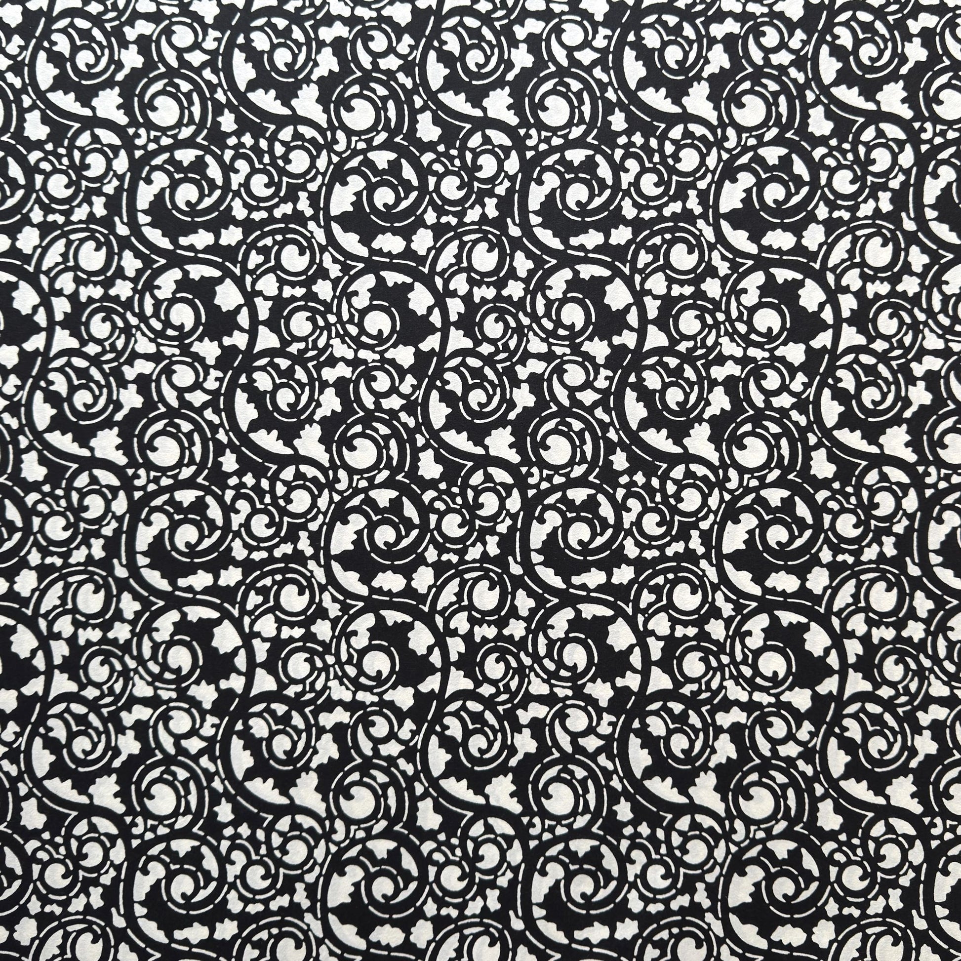 Japanese katazome-shi paper with bold black arabesque vines (karakusa) pattern on an ivory paper.