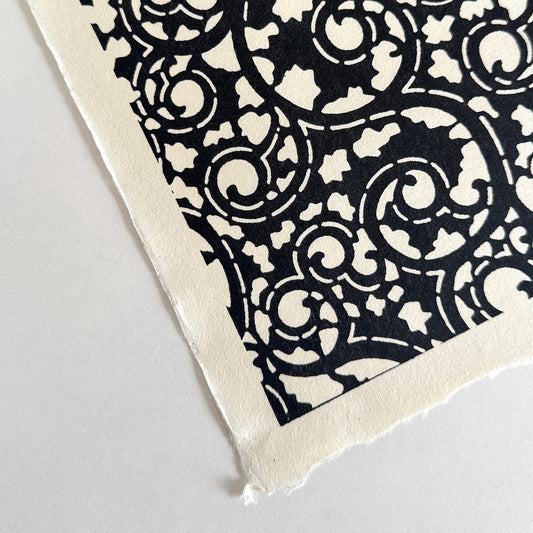 Japanese katazome-shi paper with bold black arabesque vines (karakusa) pattern on an ivory paper.  Close-up