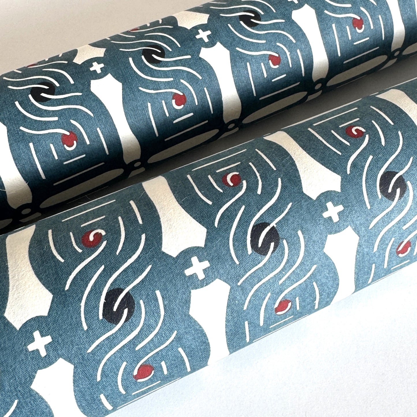 Japanese katazome stencil dyed paper with a repeat pattern of muted blue knots. Rolled and close-up