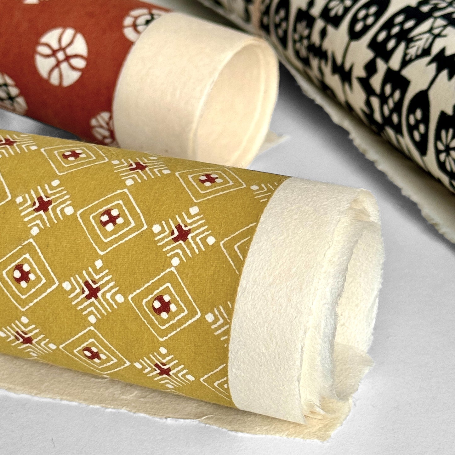 Japanese decorative stencil-dyed paper with repeat diamond pattern in a mustard gold colour. Rolled & close-up