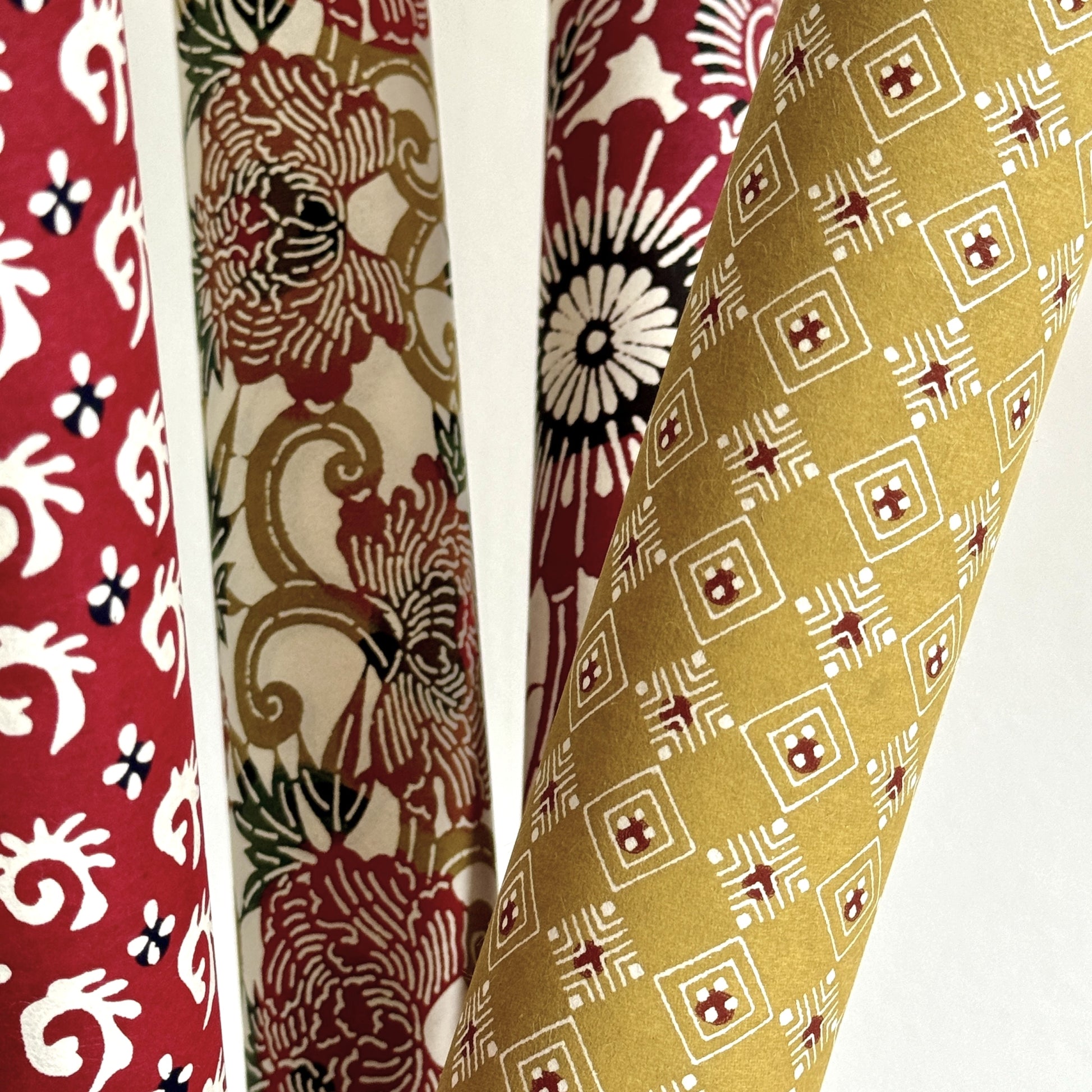 Japanese decorative stencil-dyed paper with repeat diamond pattern in a mustard gold colour. Pictured rolled with other paper designs