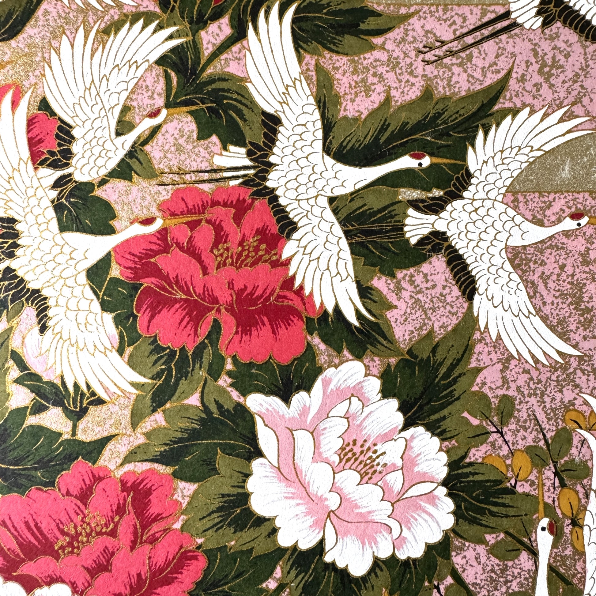 A sheet of Japanese silkscreen printed paper called Sogara which depicts white cranes flying in a pink and gold sky, surrounded by blossom and flowers. close up of the cranes