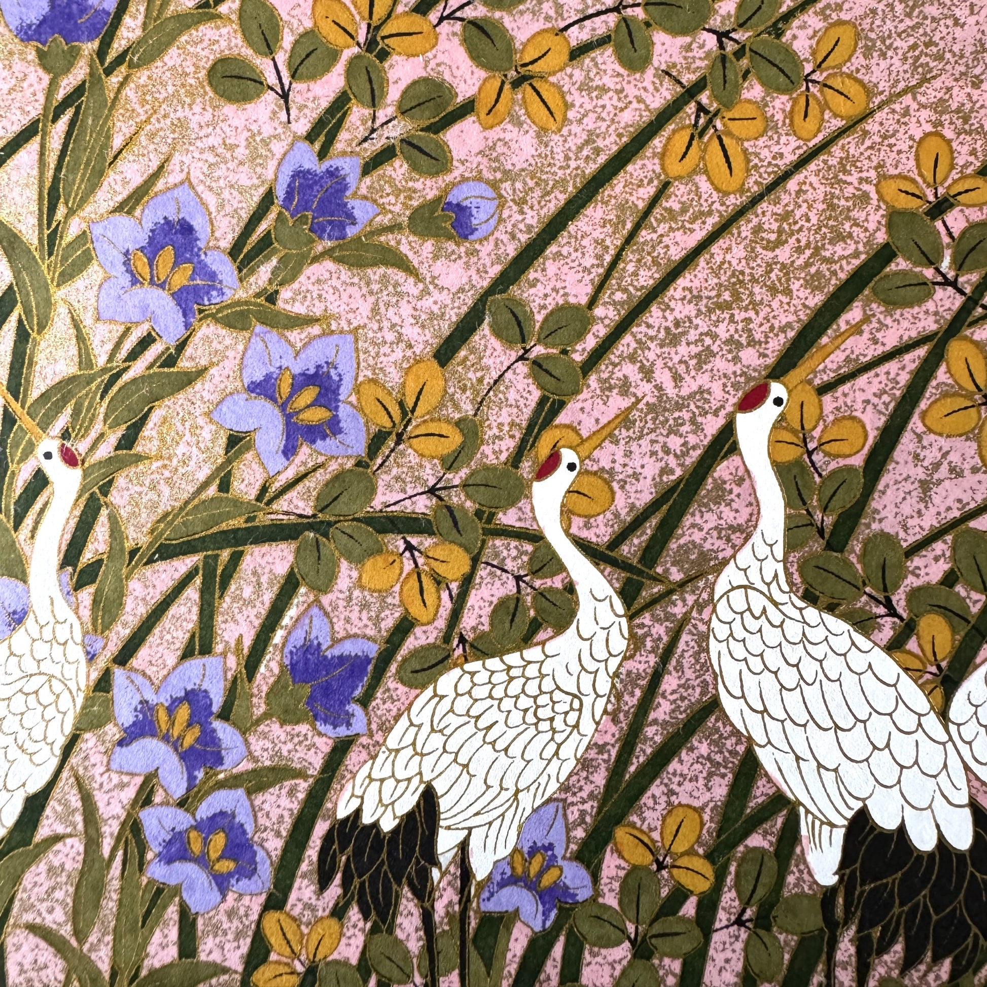A sheet of Japanese silkscreen printed paper called Sogara which depicts white cranes flying in a pink and gold sky, surrounded by blossom and flowers. Close up of two cranes standing