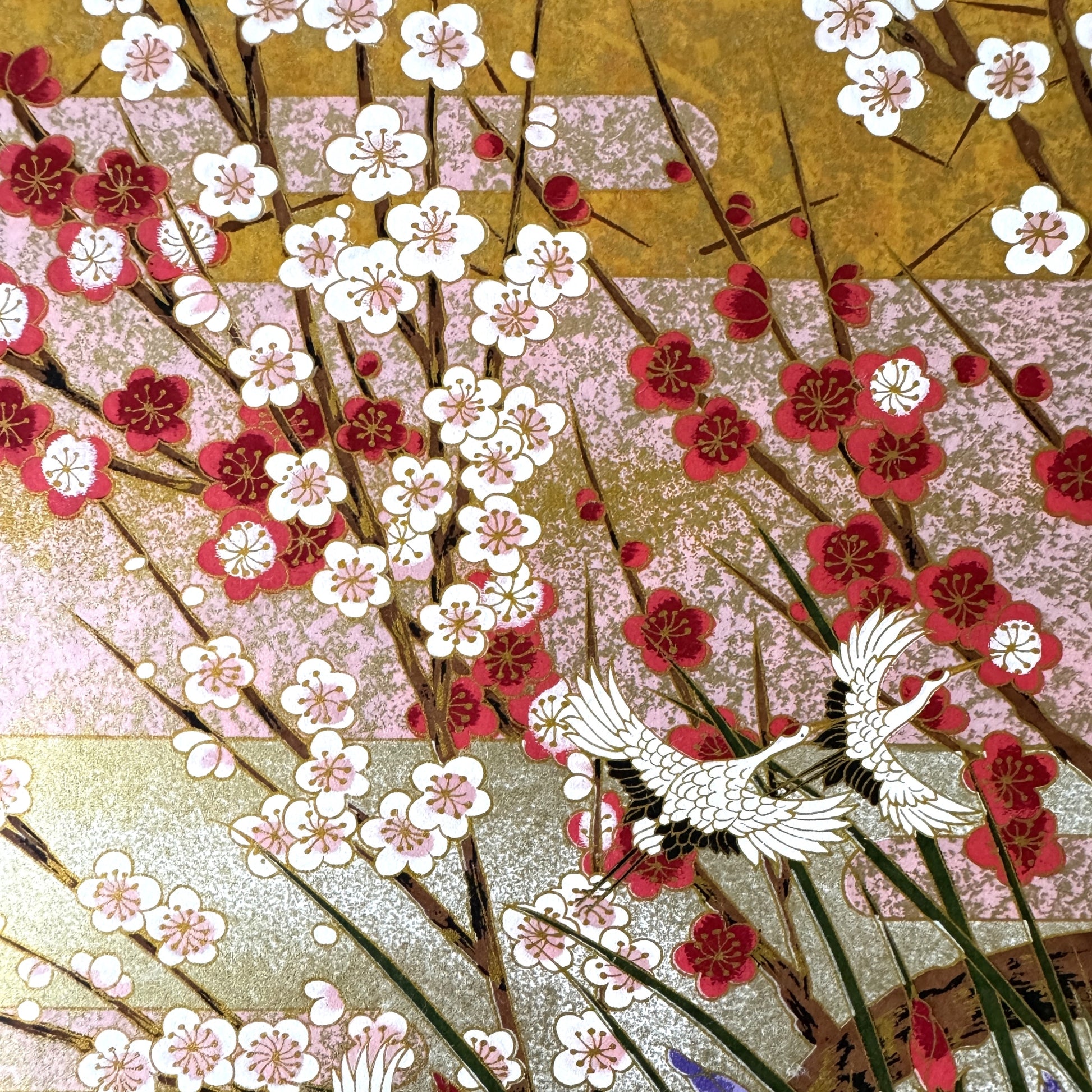 A sheet of Japanese silkscreen printed paper called Sogara which depicts white cranes flying in a pink and gold sky, surrounded by blossom and flowers. close up of plum blossom