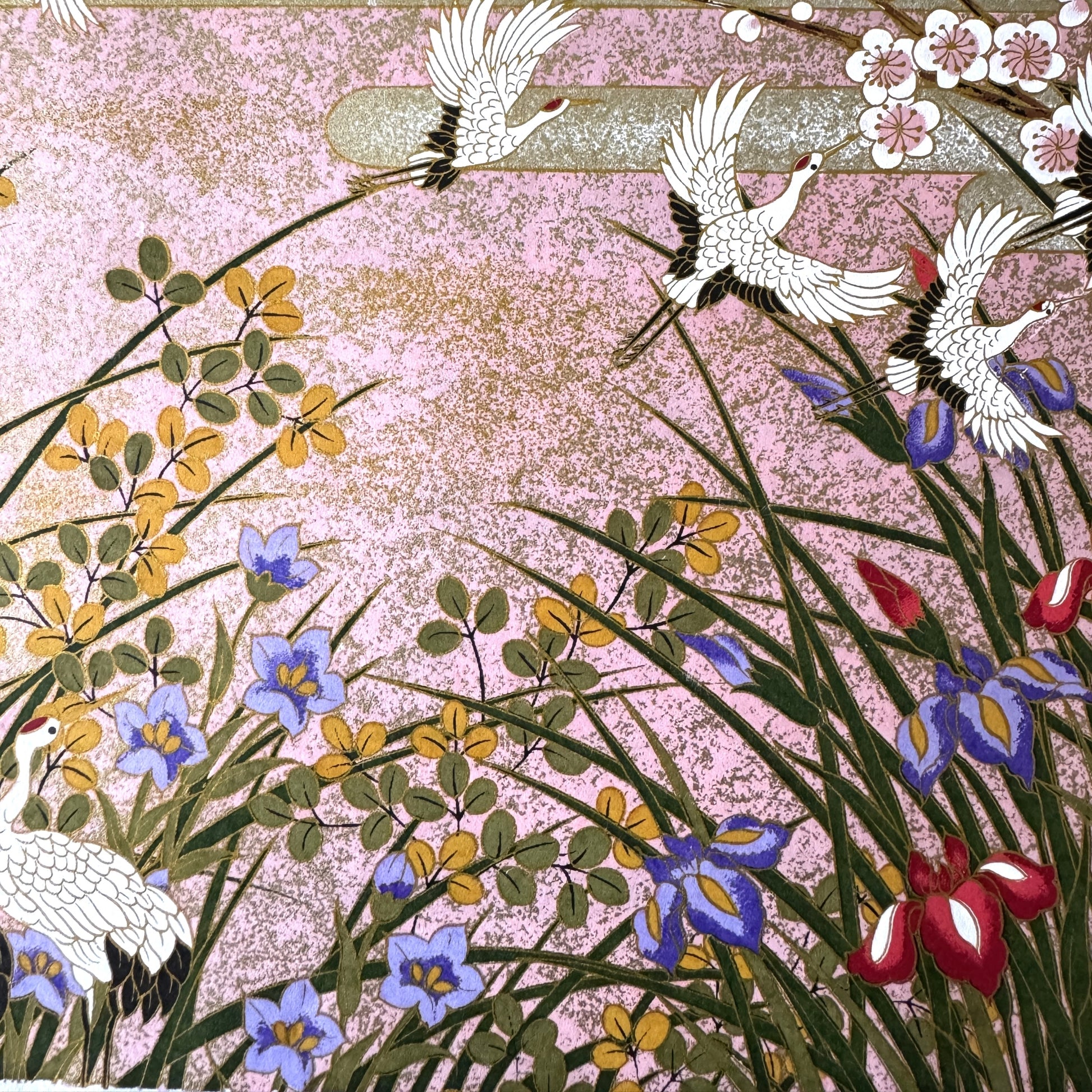 A sheet of Japanese silkscreen printed paper called Sogara which depicts white cranes flying in a pink and gold sky, surrounded by blossom and flowers. Close up of irises