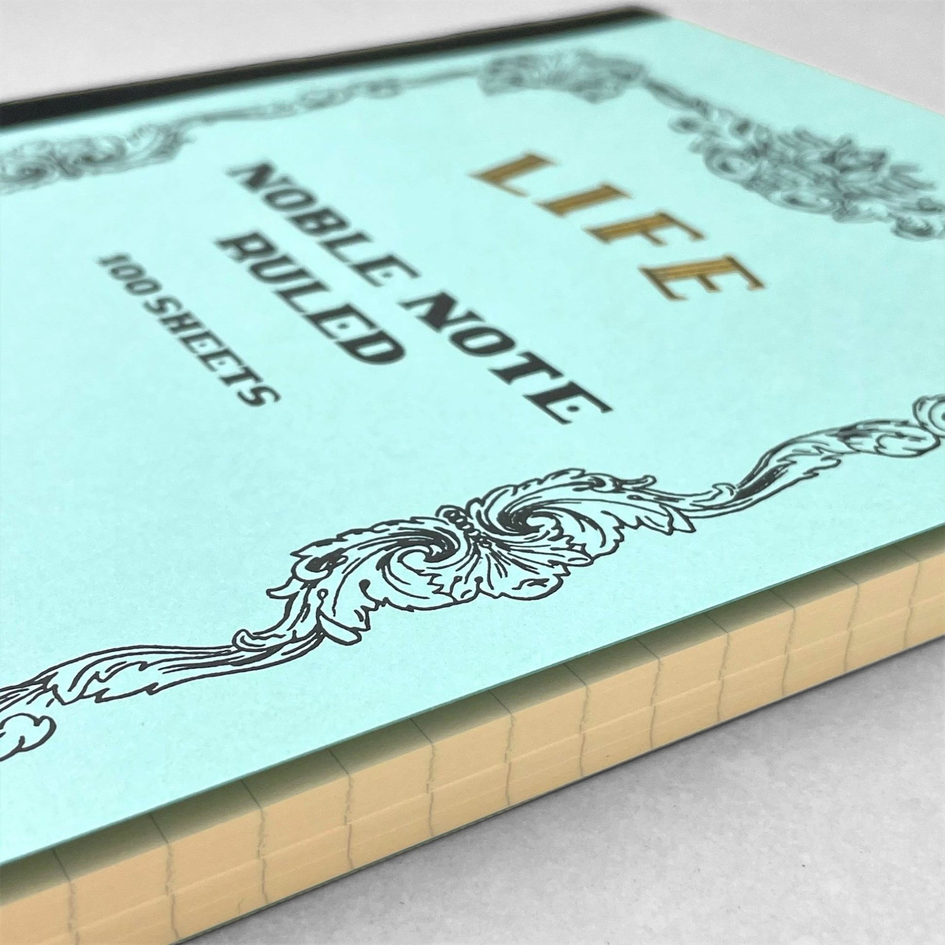 Softcover notebook with lined pages. The cover is plain aqua with a decorative black border and branding, Life Noble Ruled by Japanese brand Life