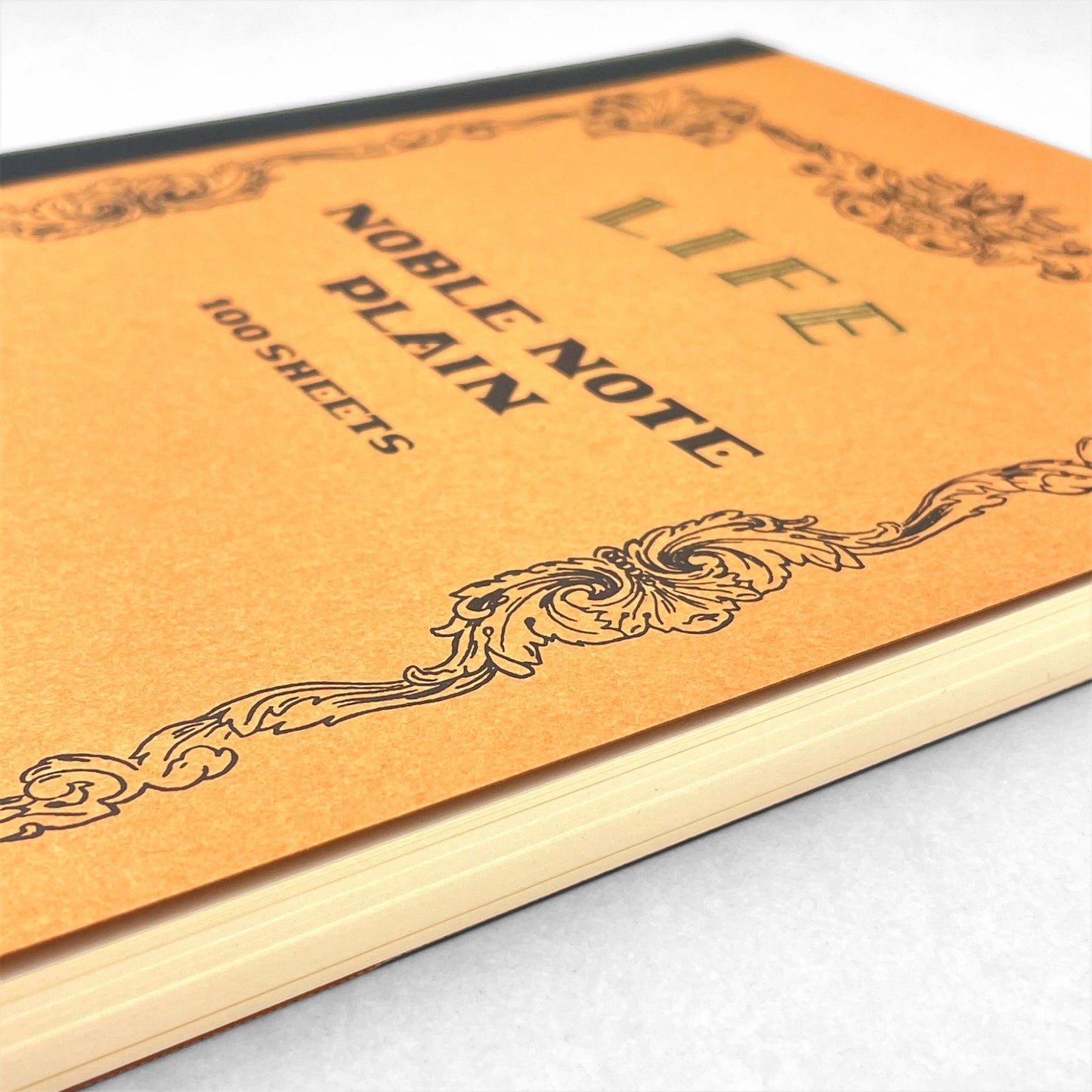 Softcover notebook with plain pages. The cover is plain ochre with a decorative black border and branding. Life Noble range by Japanese brand Life
