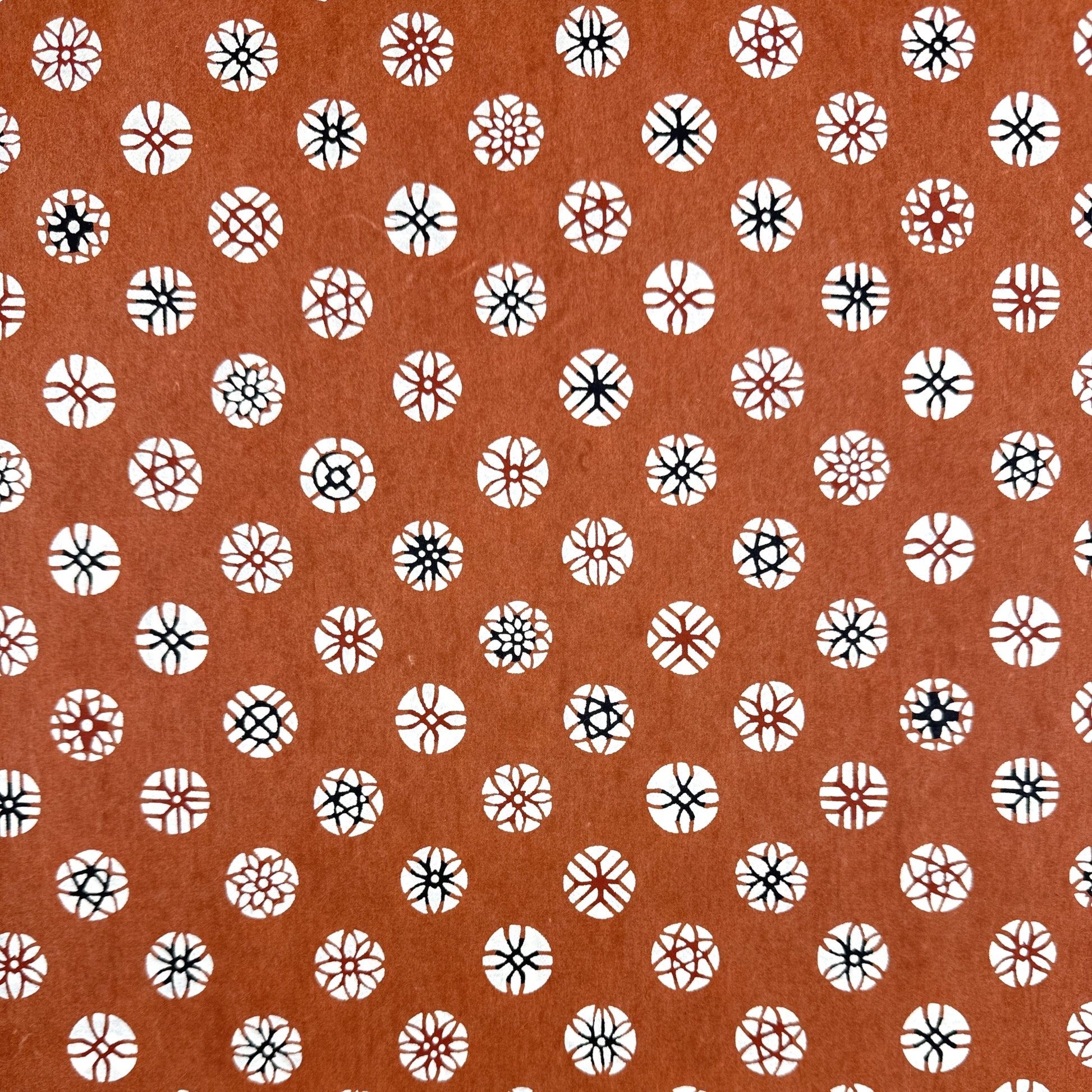 A Japanese stencil-dyed patterned paper with a repeat pattern of floral motif circles on a rich tan brown base