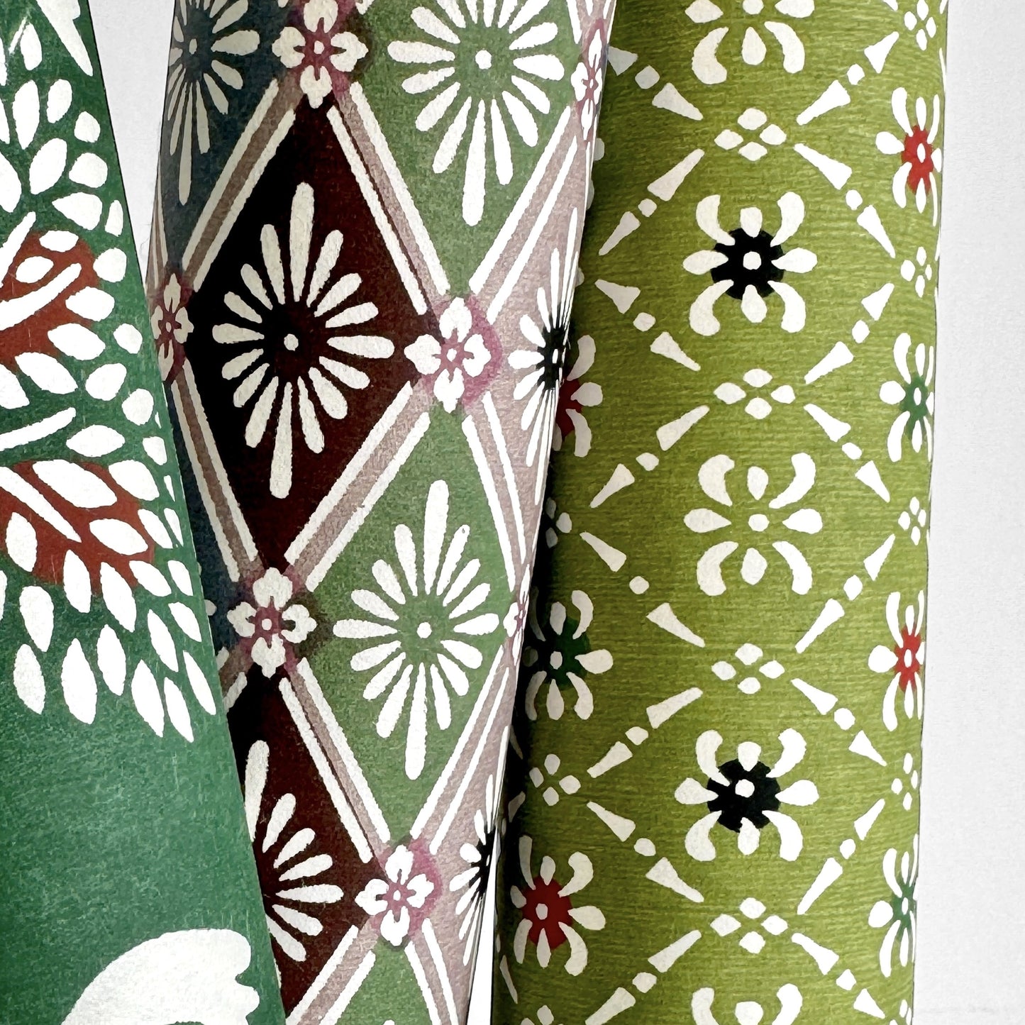 Japanese stencil-dyed katazome-shi paper with a white geometric pattern on green backdrop. Pictured rolled with other designs