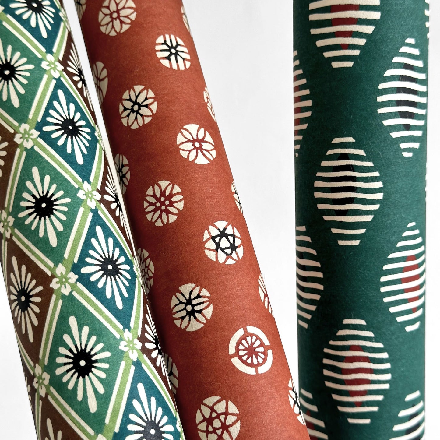 A Japanese stencil-dyed patterned paper with a repeat pattern of floral diamonds in tones of blue, aqua, brown and white. Pictured rolled with other designs.