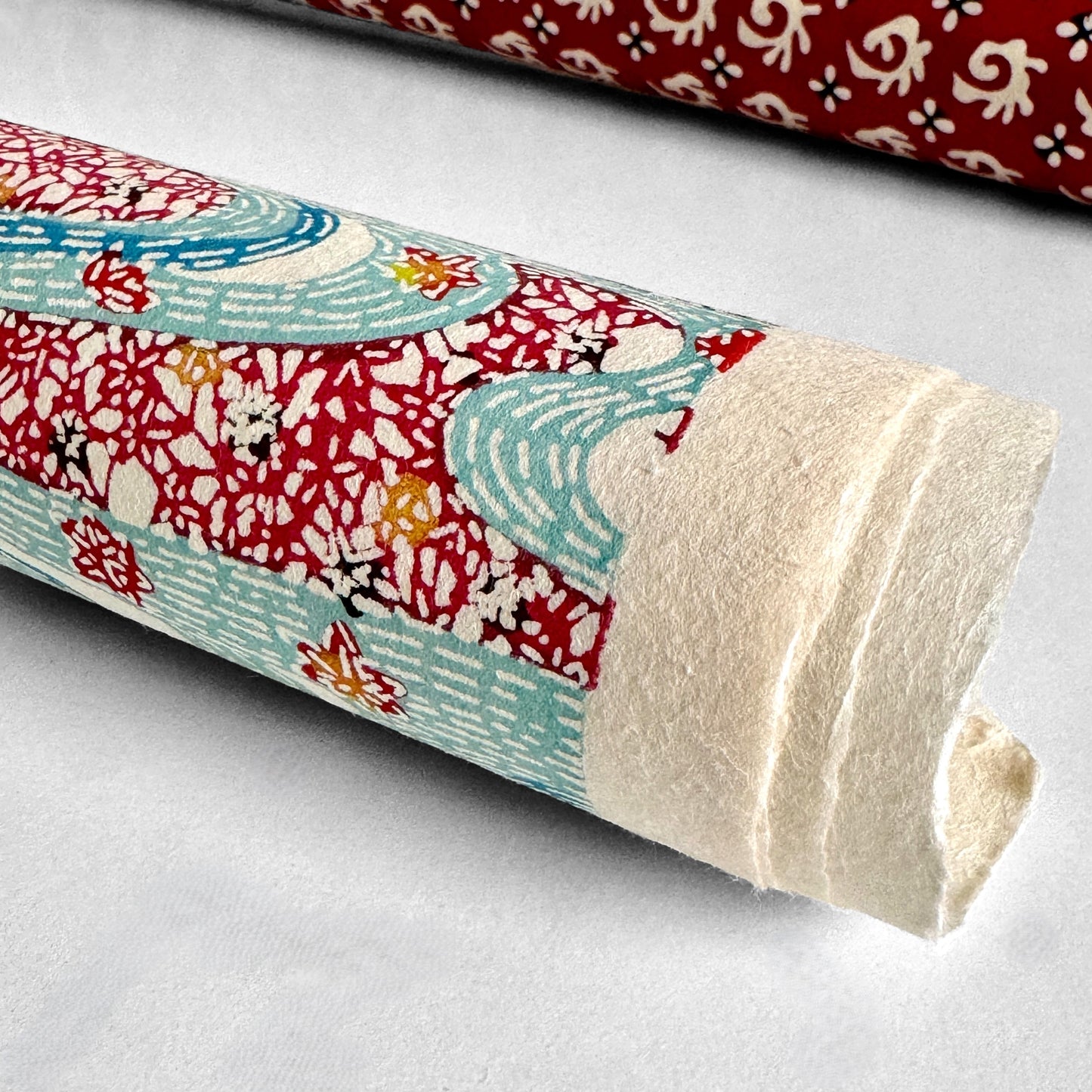 Japanese stencil-dyed paper with a pattern of a stylised blue river and dark red banks of flowers. Rolled & close up