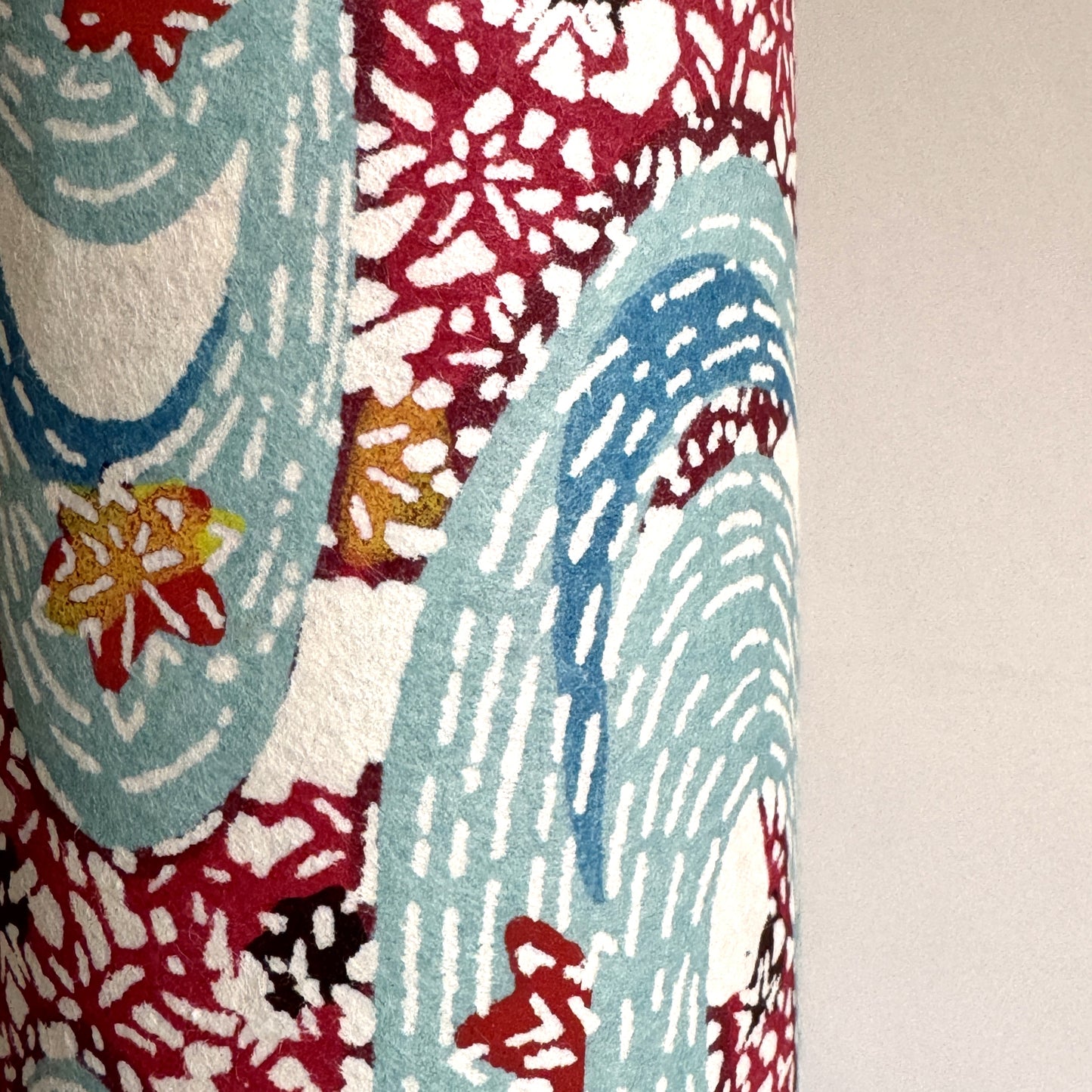 Japanese stencil-dyed paper with a pattern of a stylised blue river and dark red banks of flowers. Close-up