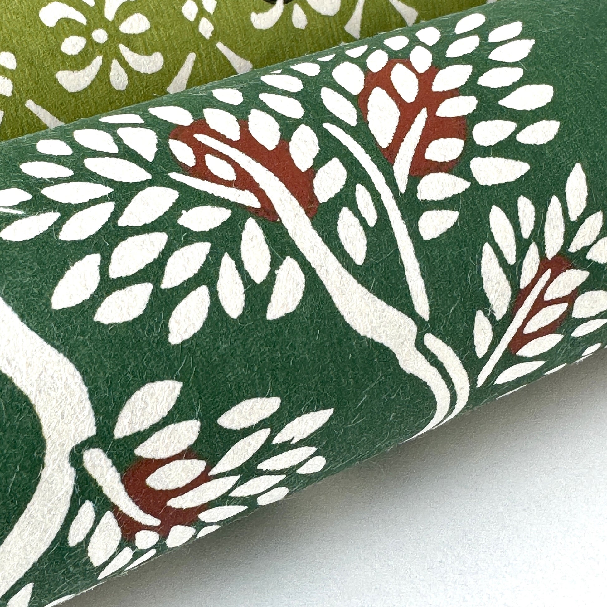 A Japanese stencil-dyed patterned paper in dark green with a repeat pattern of white bonsai trees. Close-up, rolled