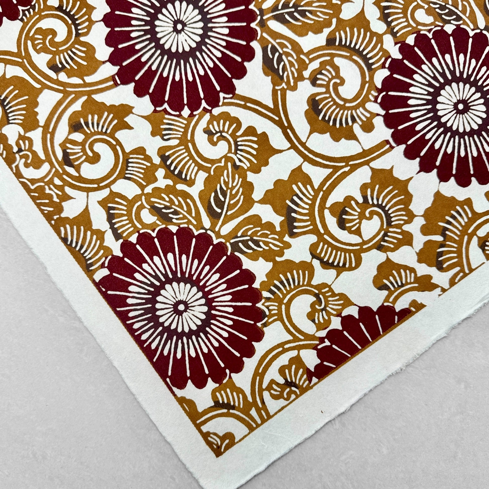 Japanese stencil-dyed paper with a large stylised floral pattern of a chrysanthemum in deep brown and tan. Close-up