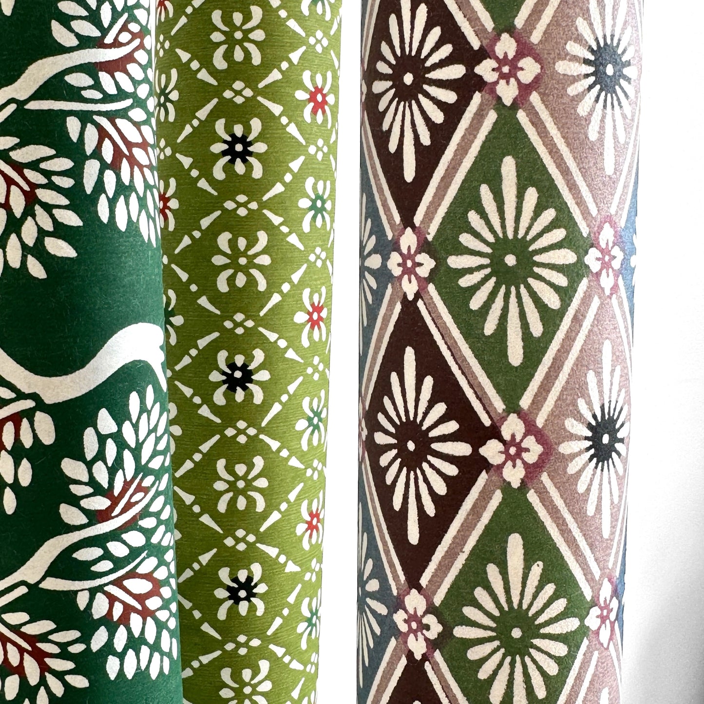 A Japanese stencil-dyed patterned paper with a repeat diamond floral pattern in blue, taupe, green and brown. Pictured rolled with other designs