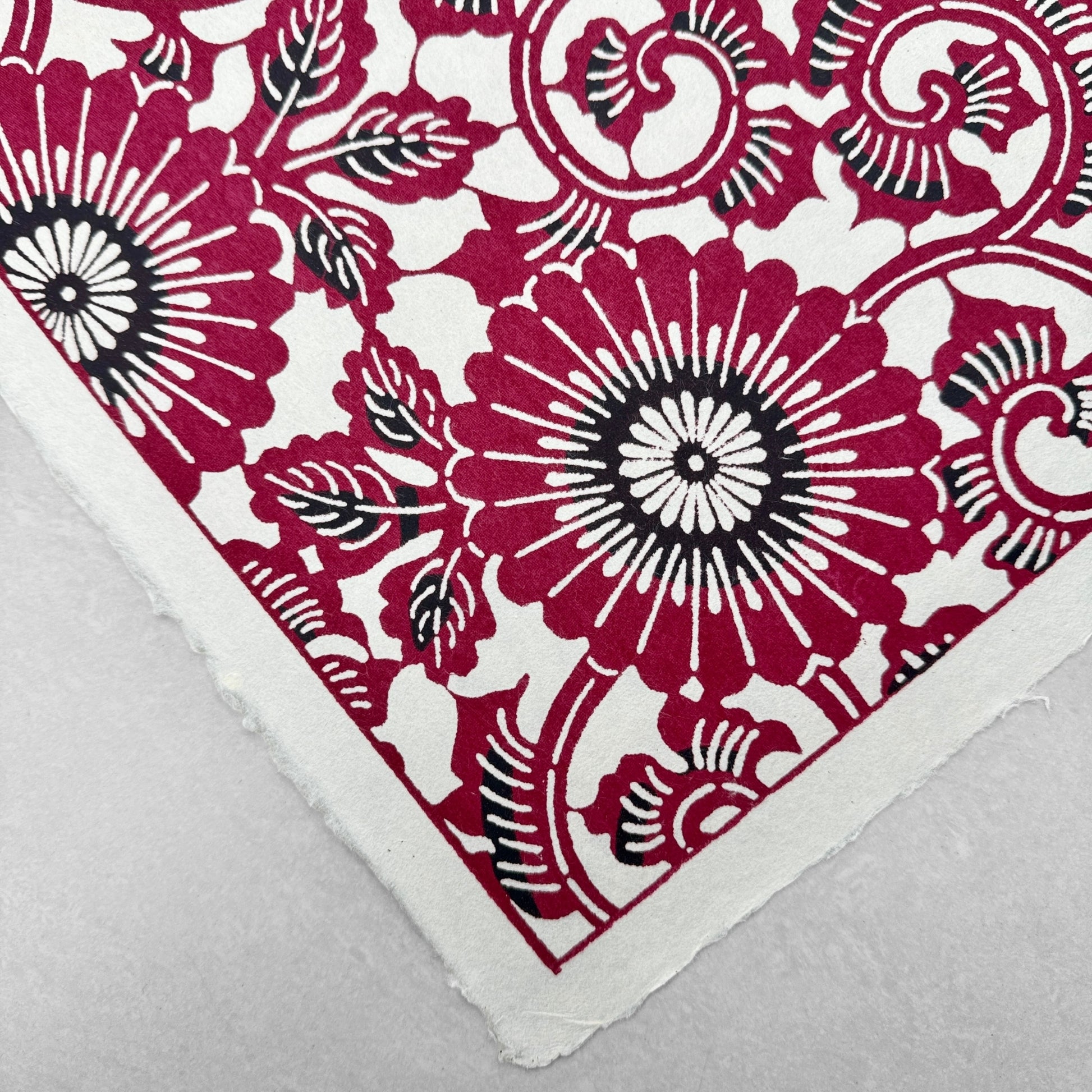 Japanese stencil-dyed paper with a repeat pattern of chrysanthemum flowers and swirling vines in deep berry red, closeup