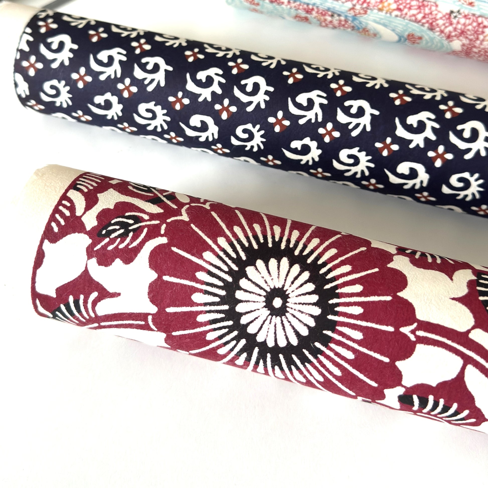 Japanese stencil-dyed paper with a repeat pattern of chrysanthemum flowers and swirling vines in deep berry red. Pictured rolled