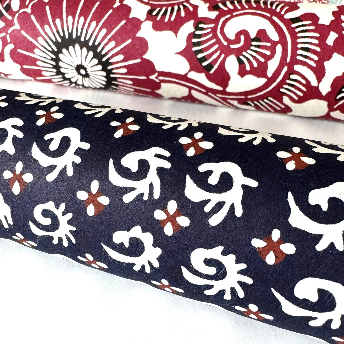 japanese stencil-dyed paper with a white swirl geometric repeat pattern on a dark inky blue background. Pictured rolled