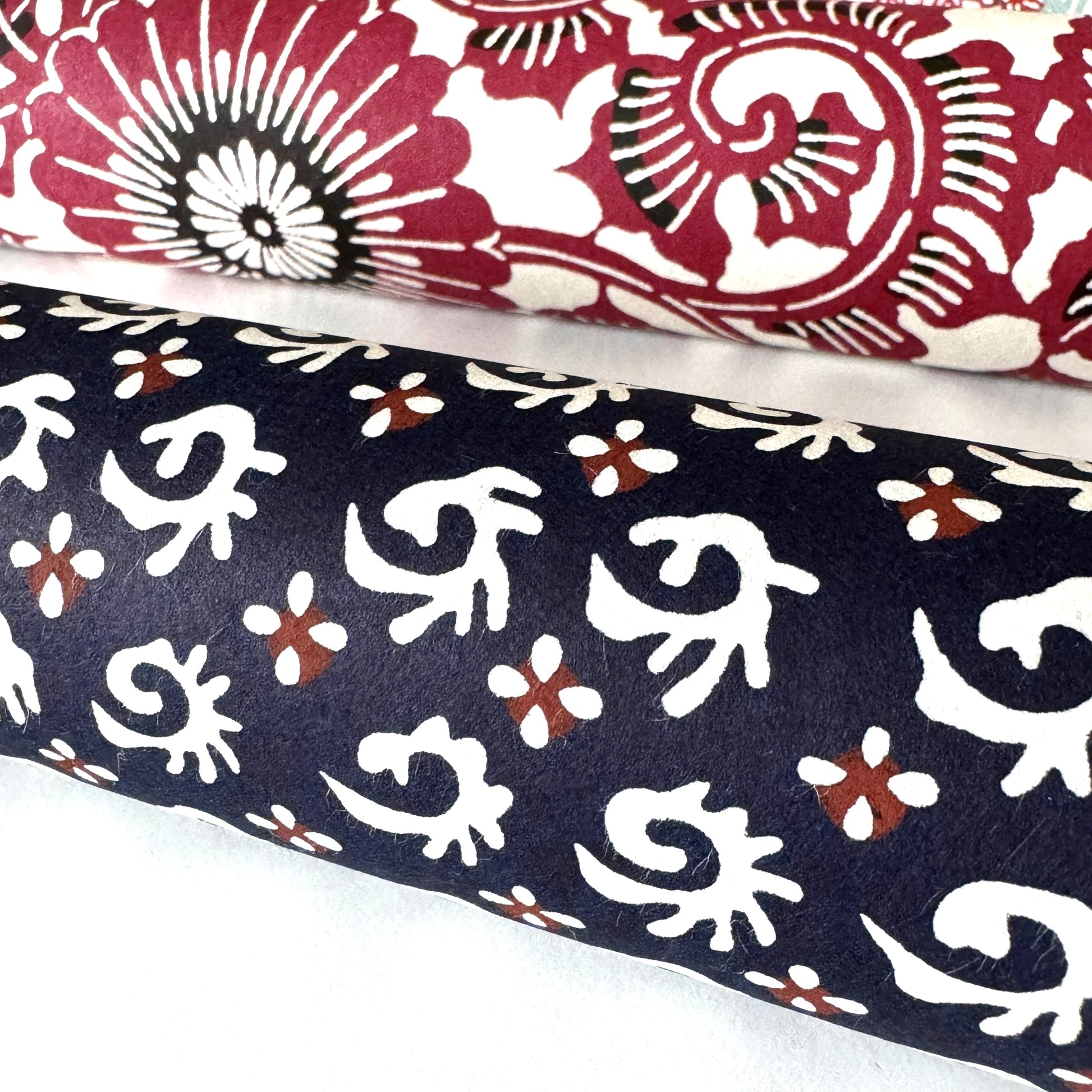 japanese stencil-dyed paper with a white swirl geometric repeat pattern on a dark inky blue background. Pictured rolled