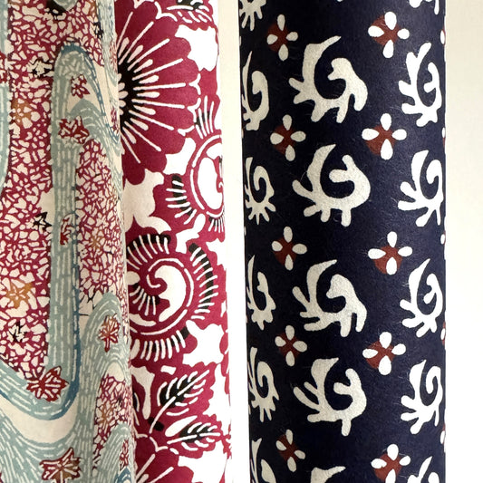japanese stencil-dyed paper with a white swirl geometric repeat pattern on a dark inky blue background. Pictured rolled with other paper designs