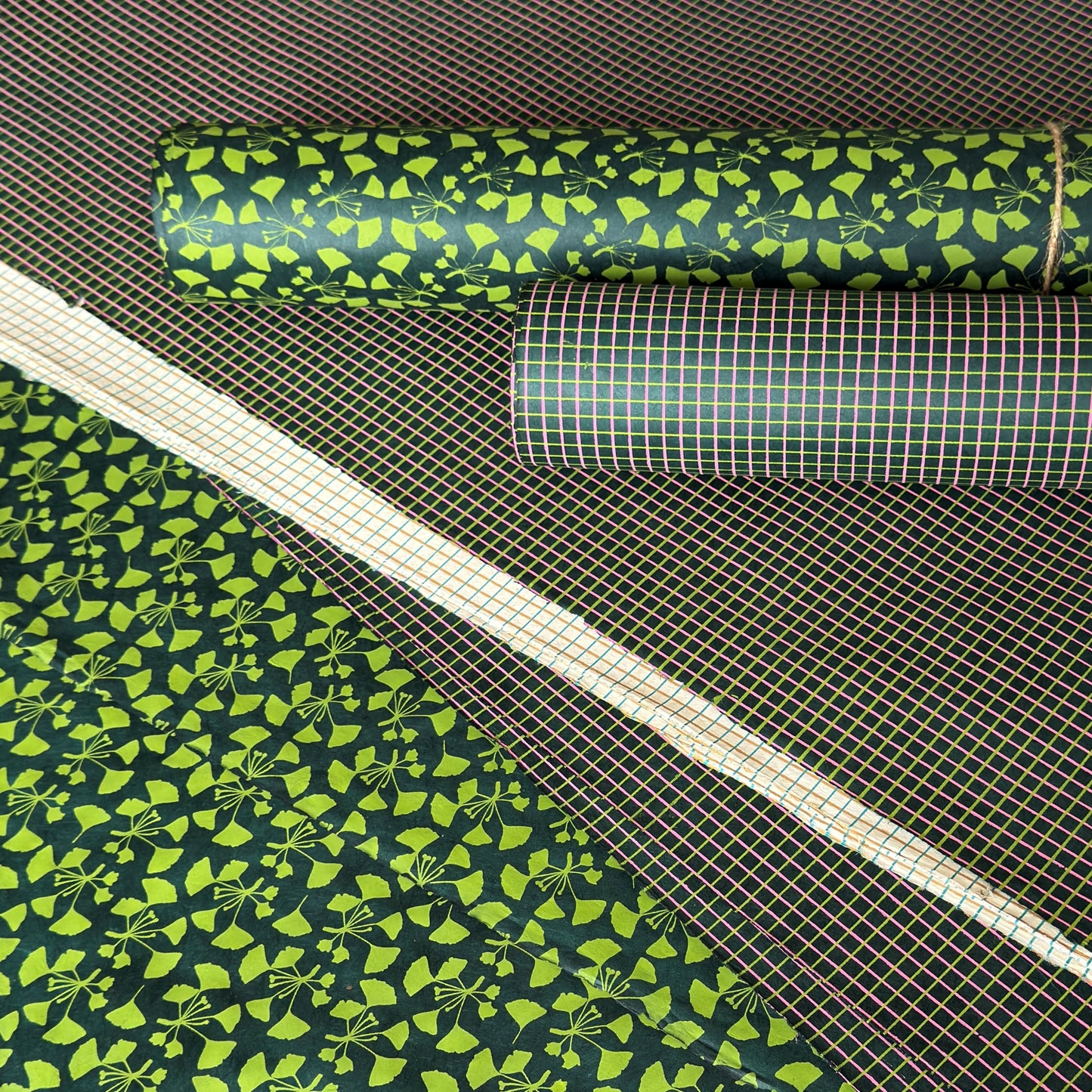 a sheet of Nepalese lokta paper with a lime green and pink grid pattern on dark green handmade paper. Pictured alongside a floral paper
