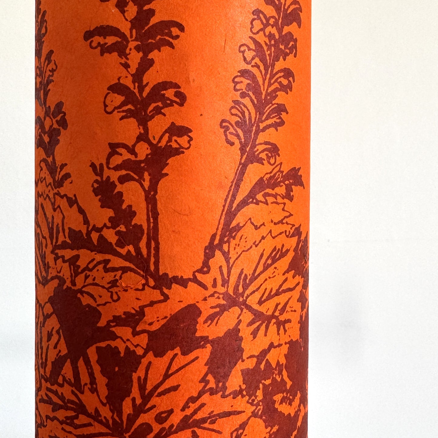 Nepalese handmade decorative lokta paper sheet with a Toile de Jouy style pattern of an agapanthus flower in burgundy screen printed on an orange lokta paper. close-up