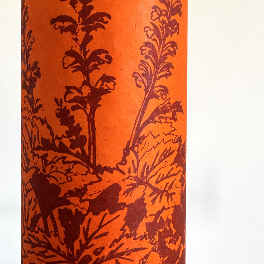 Nepalese handmade decorative lokta paper sheet with a Toile de Jouy style pattern of an agapanthus flower in burgundy screen printed on an orange lokta paper. close-up