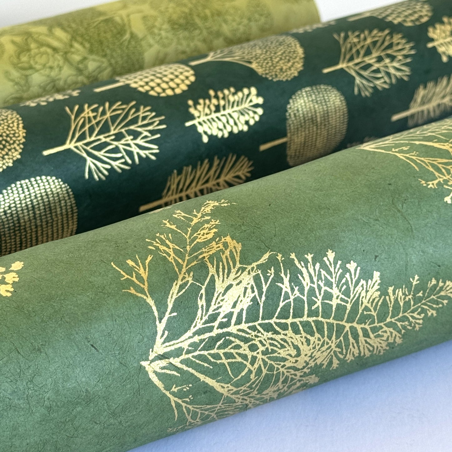 Nepalese handmade decorative lokta paper sheet with gold leaves screen printed on a green lokta paper. Close up rolled