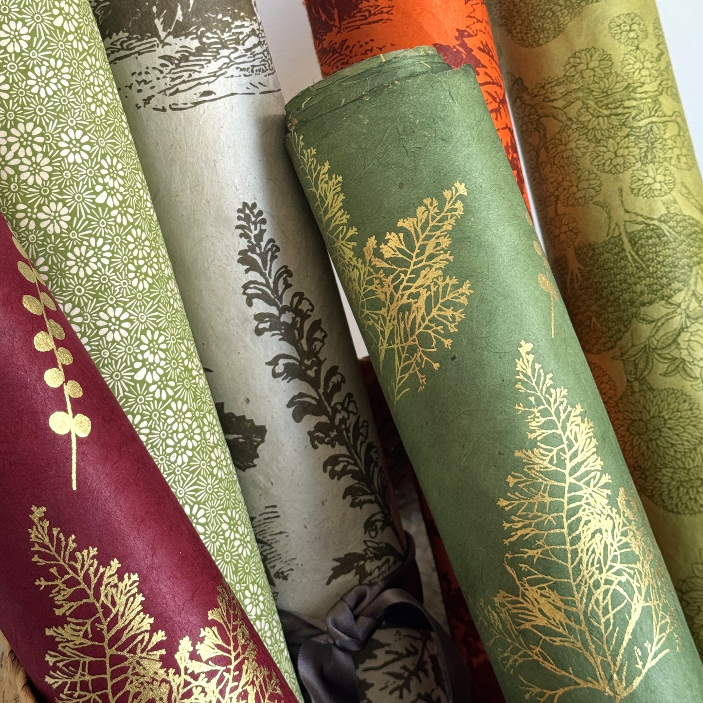 Nepalese handmade decorative lokta paper sheet with gold leaves screen printed on a green lokta paper. Pictured with other botanical designs from the collection.