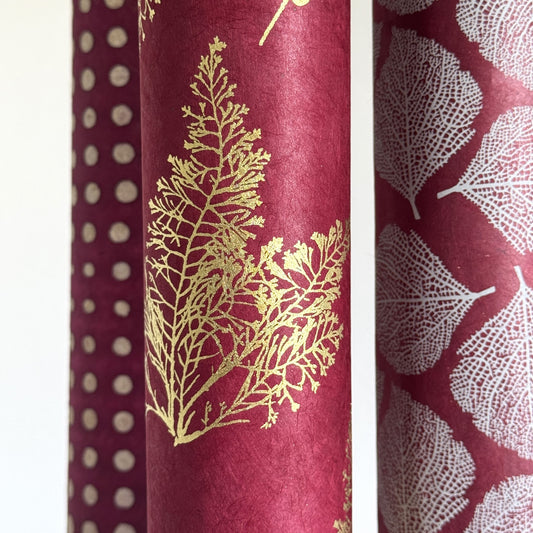 Nepalese handmade decorative lokta paper sheet with gold leaves screen printed on a burgundy red lokta paper, close up