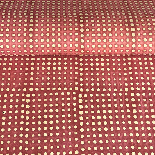 a sheet of Nepalese batik lokta paper in coral rose colour with a repeat white dot design.