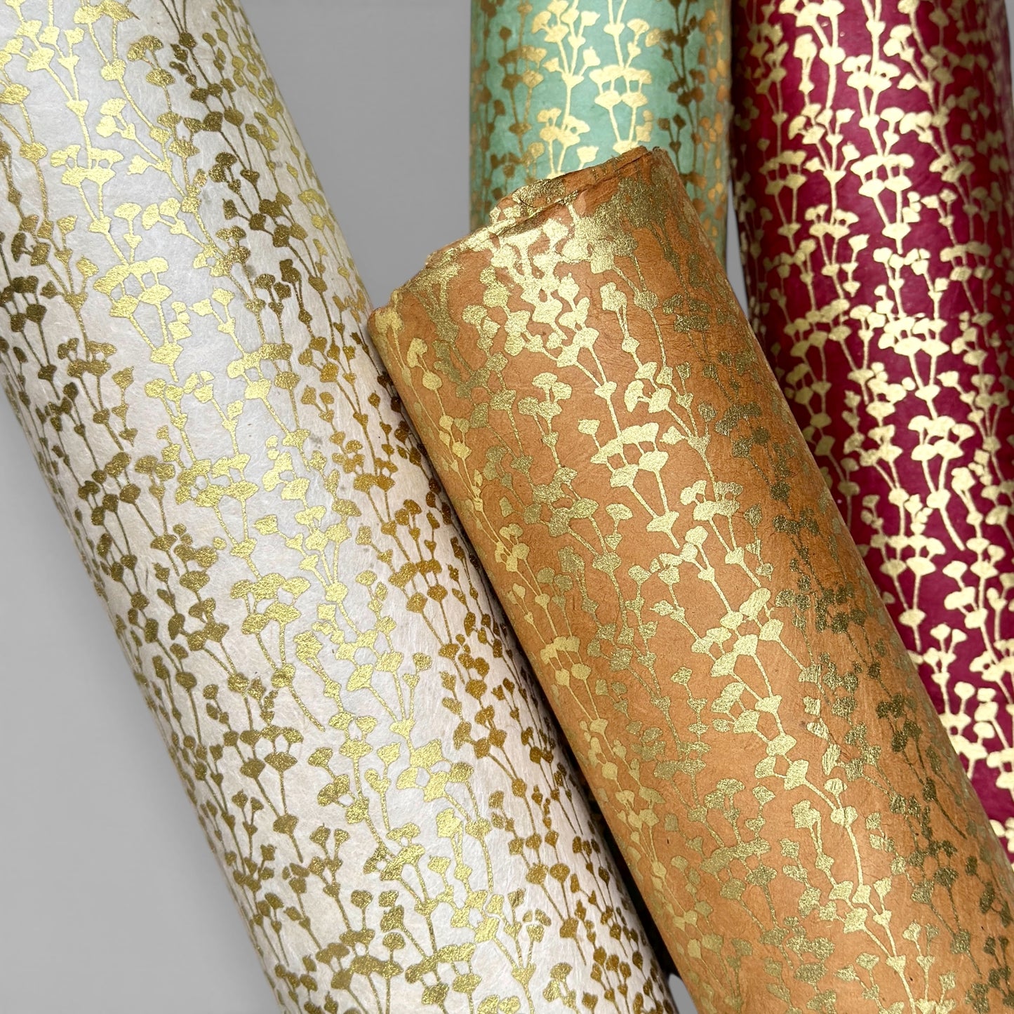 nepalese hand printed lokta paper with a small gold abstract gingko design pictured rolled in four different colours -white, tan, green and red