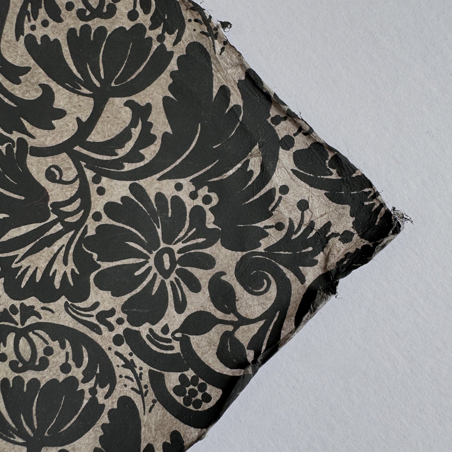 Nepalese handmade decorative lokta paper sheet with a black floral pattern screen printed on a dark taupe lokta paper. Close up of the deckle edge