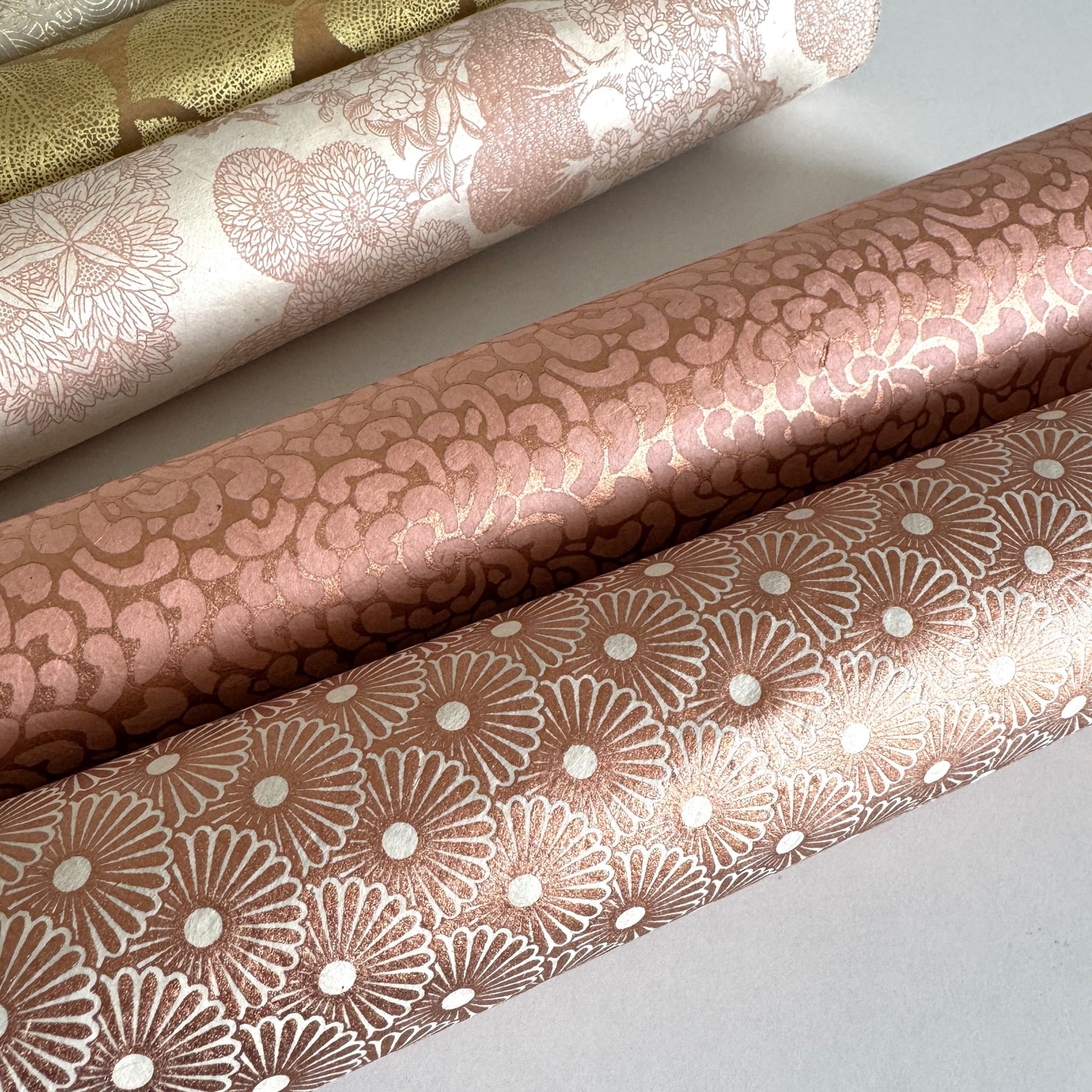 Nepalese handmade decorative lokta paper sheet with a copper metallic repeat floral pattern screen printed on an ivory lokta paper. Rolled with other designs