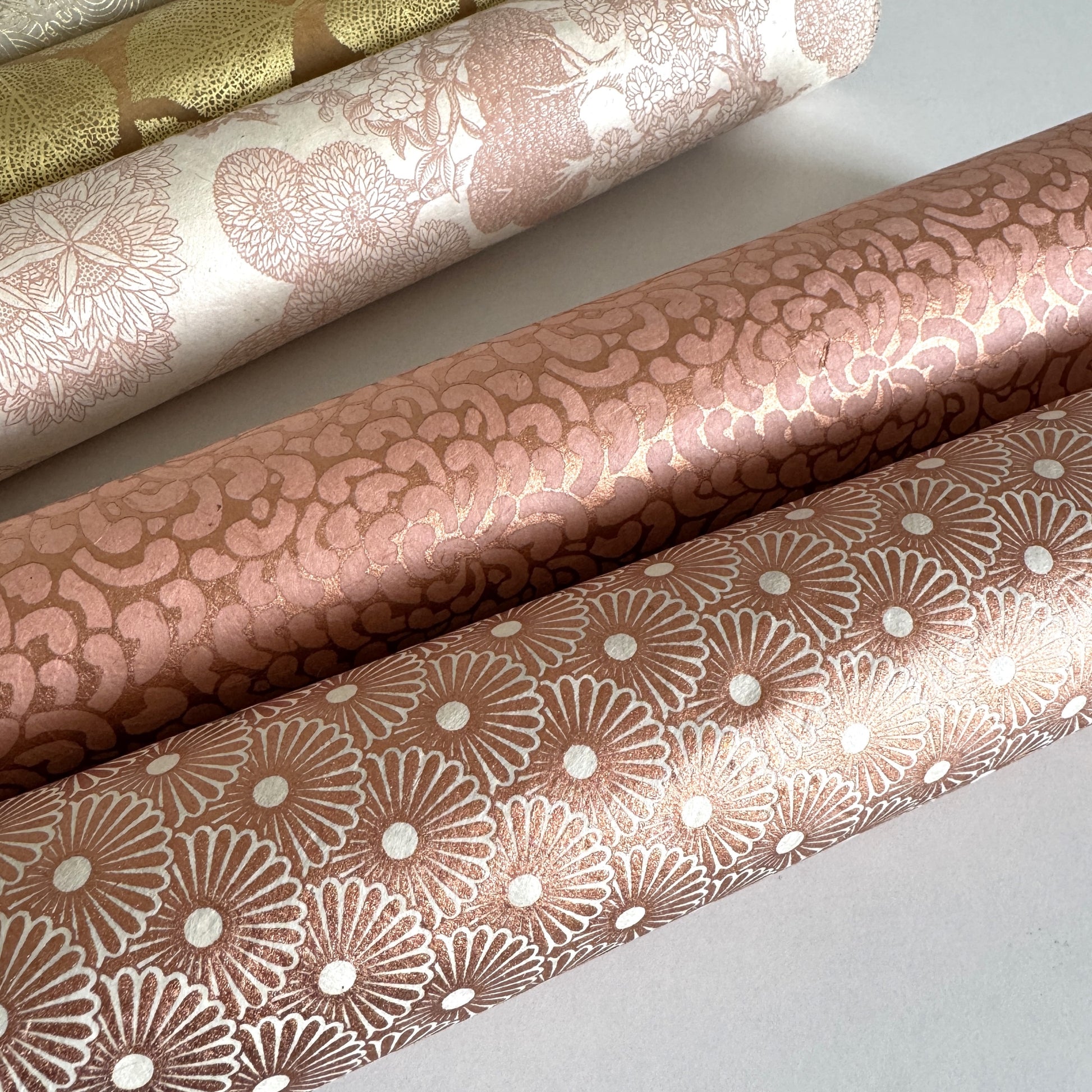 Nepalese handmade decorative lokta paper sheet with a copper metallic repeat floral pattern screen printed on an ivory lokta paper. Rolled with other designs