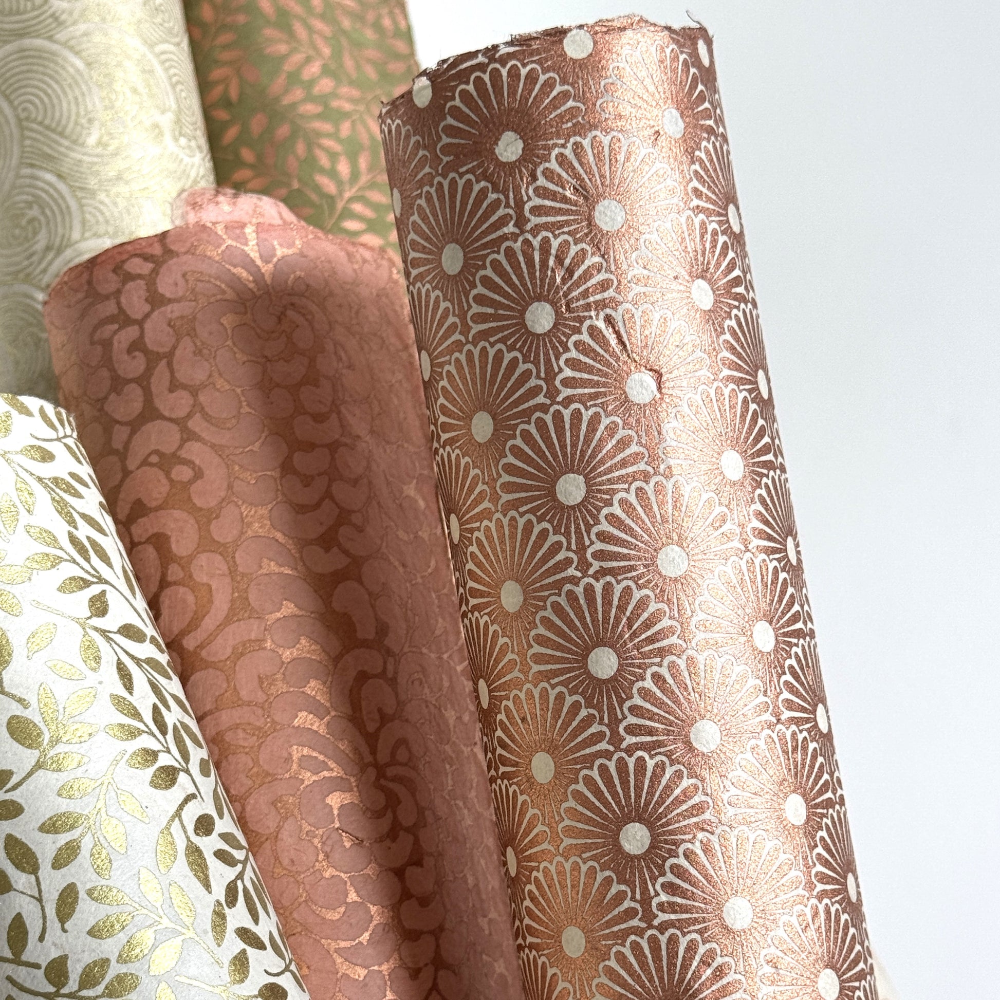 Nepalese handmade decorative lokta paper sheet with a copper metallic repeat floral pattern screen printed on an ivory lokta paper. Rolled with other designs