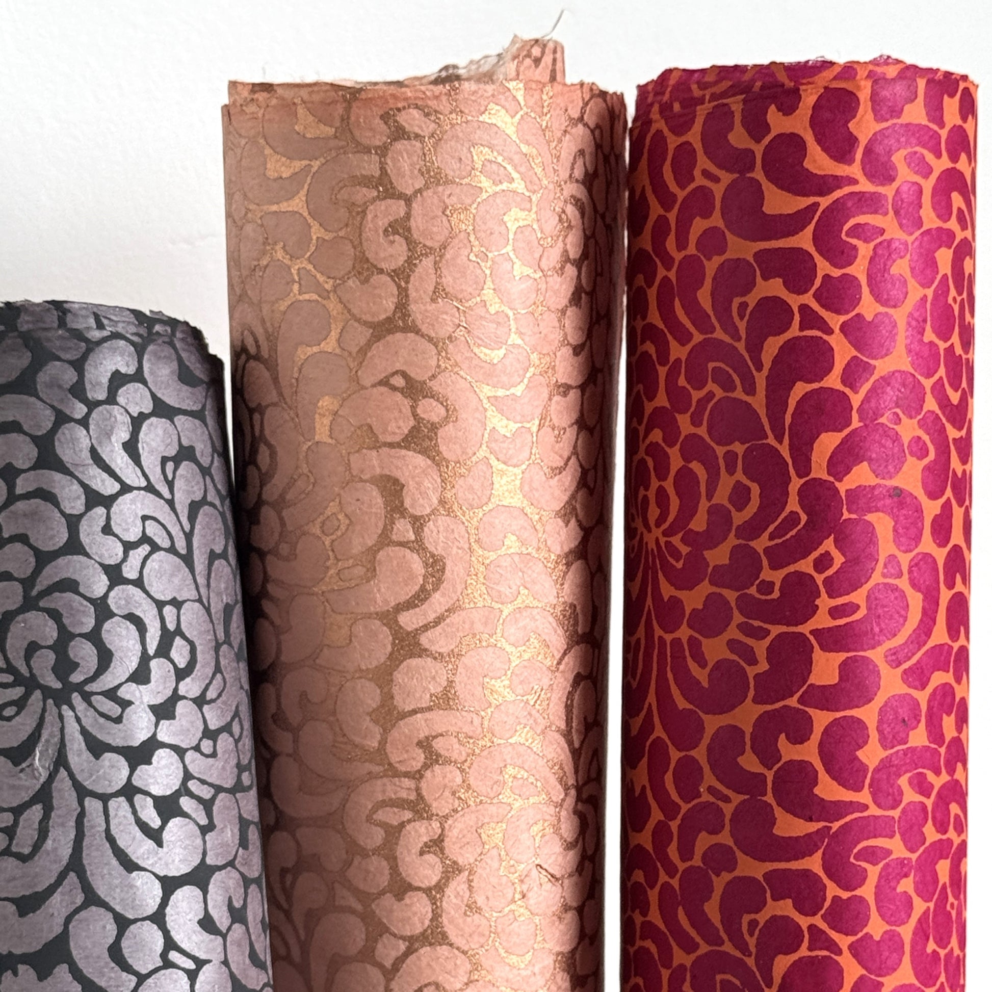 Nepalese handmade lokta paper sheet with a screen printed coral floral design on fuchsia lokta paper. Pictured rolled with other colours of the same design.