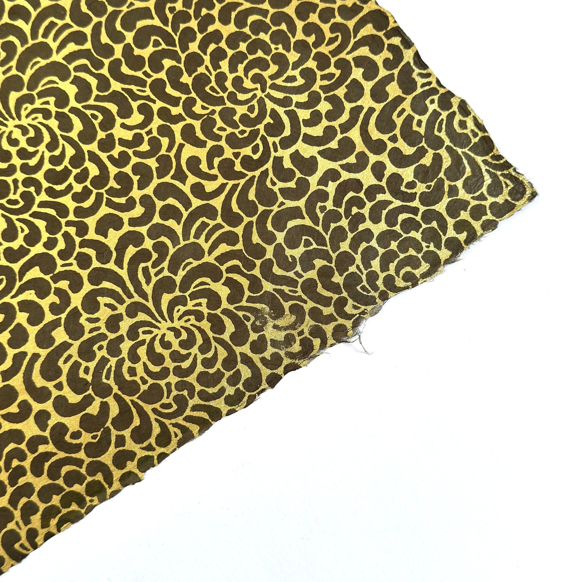 Nepalese handmade decorative lokta paper sheet with a gold screen printed floral design on a brown dyed lokta paper. Showing the deckled edge