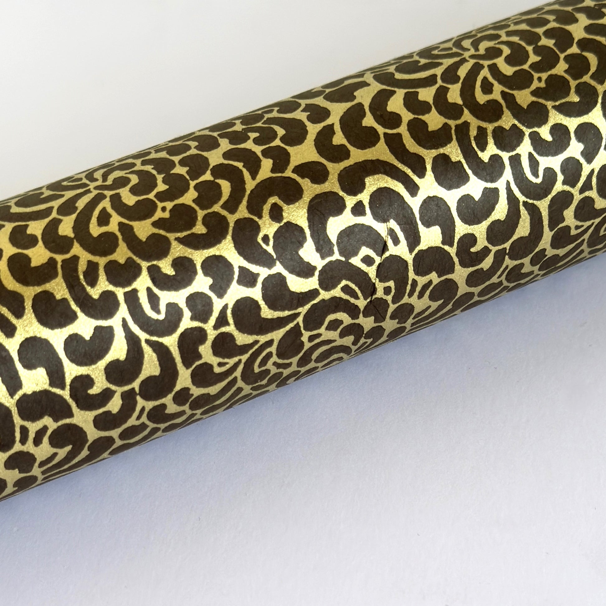 Nepalese handmade decorative lokta paper sheet with a gold screen printed floral design on a brown dyed lokta paper. Pictured rolled