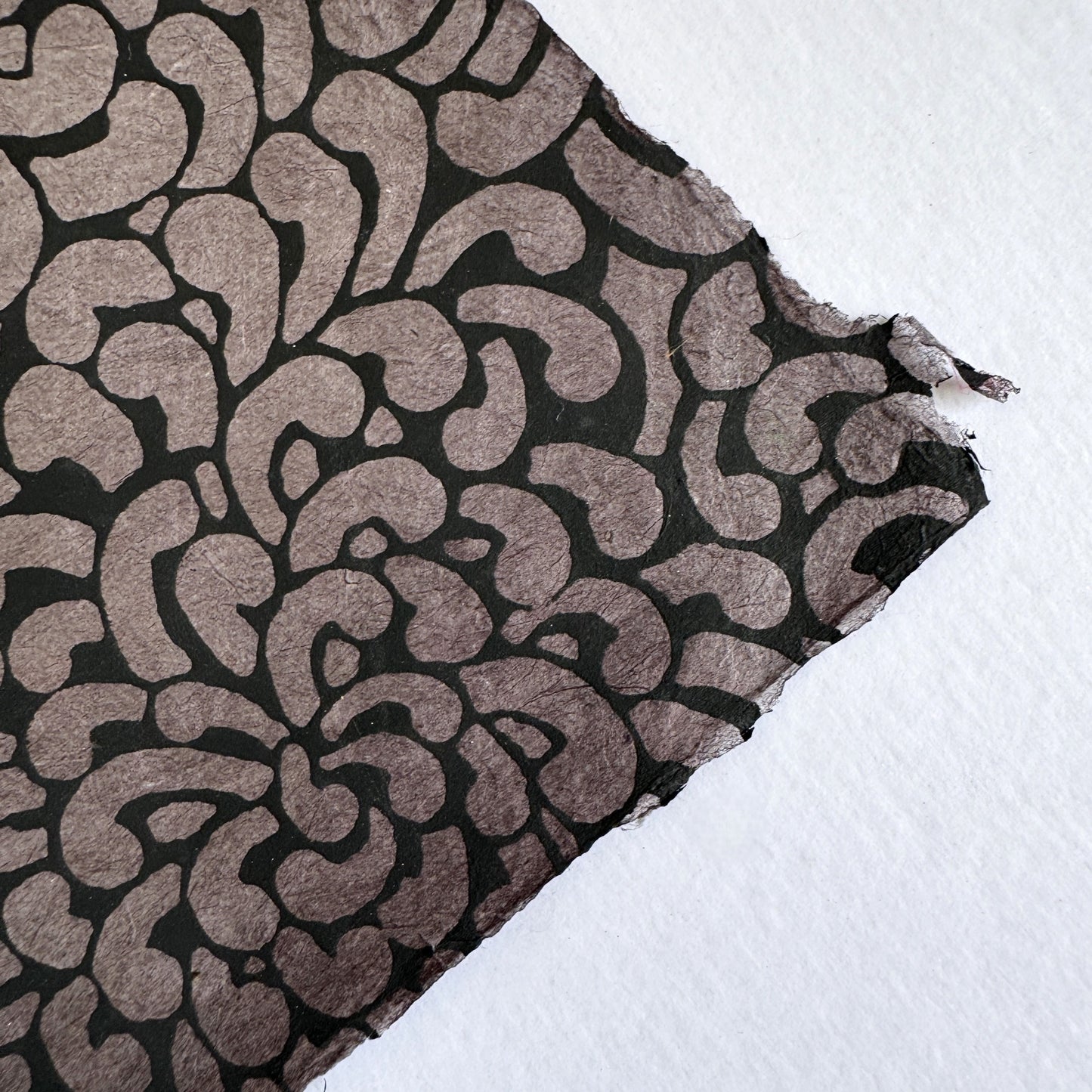 Nepalese handmade lokta paper sheet with a screen printed black floral design on slate lokta paper. Close up of the deckled edge