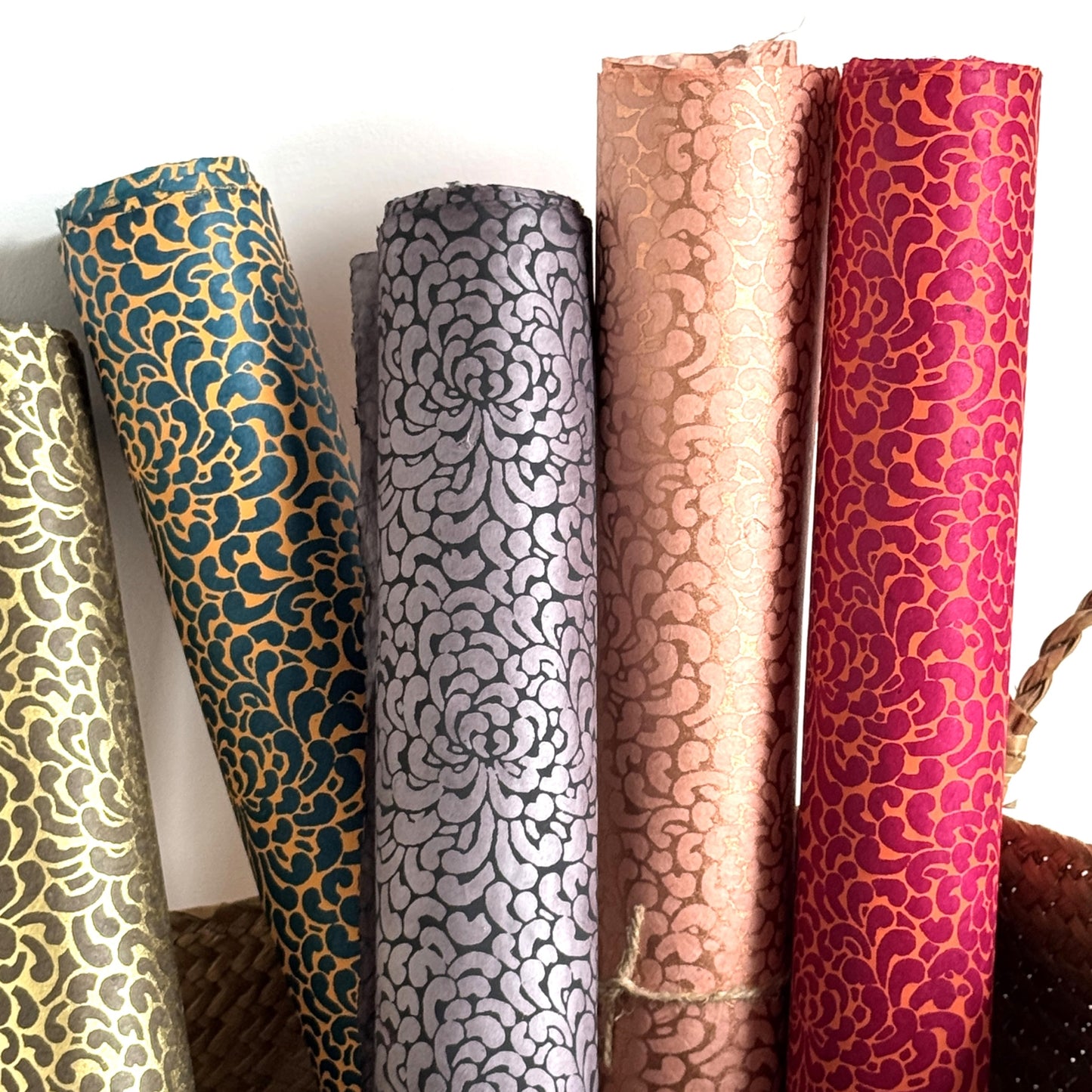 Nepalese handmade decorative lokta paper sheet with a saffron floral print screen printed on a teal lokta paper. Pictured rolled with other colours in the collection.