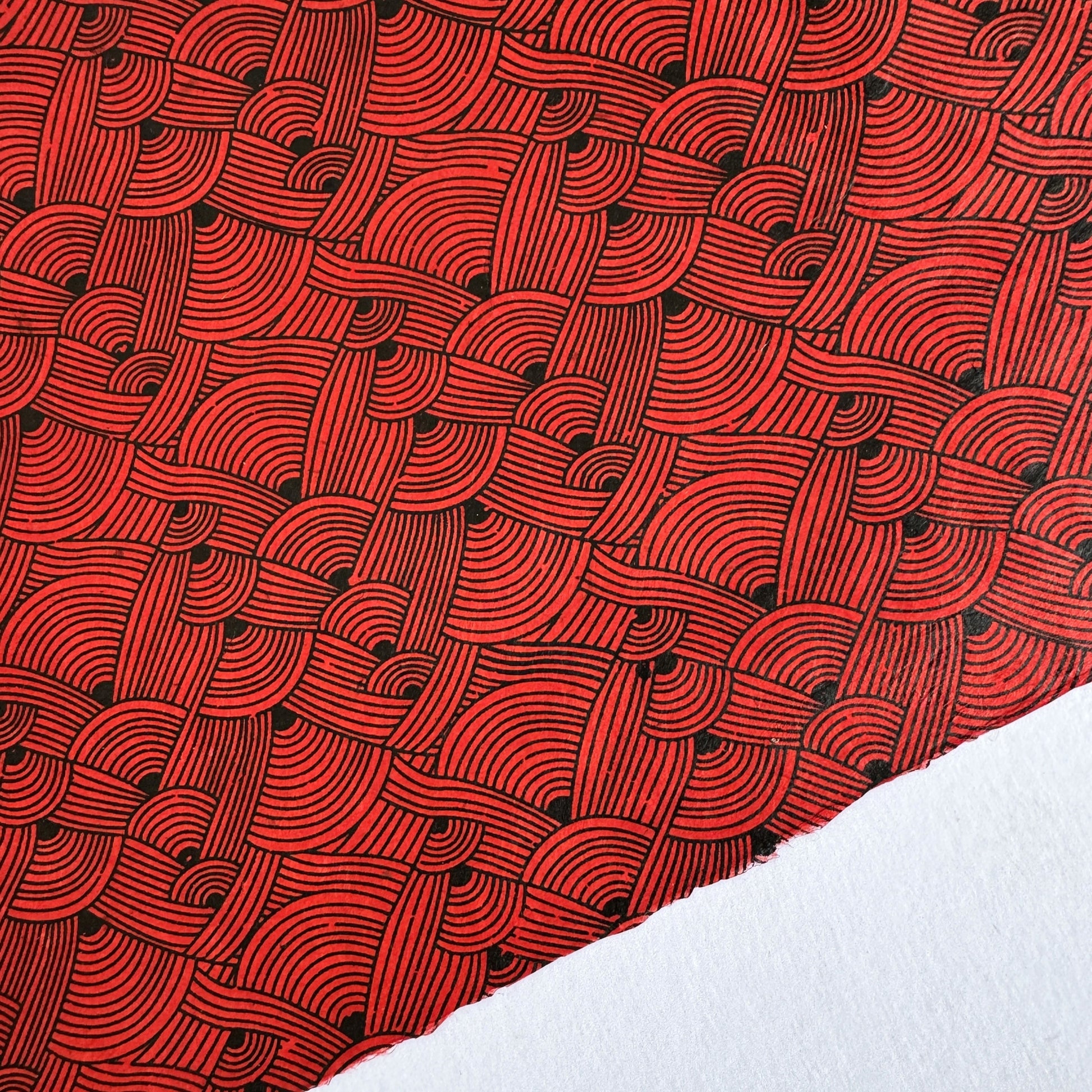 Nepalese handmade decorative lokta paper sheet with a fine lined black knots pattern screen printed on a red lokta paper.