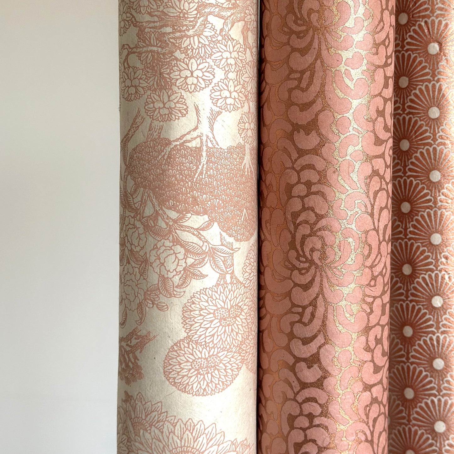 Nepalese handmade decorative lokta paper sheet with a detailed design of trees and flowers in blush pink screen printed on an ivory lokta paper. Rolled alongside other blush pink patterns