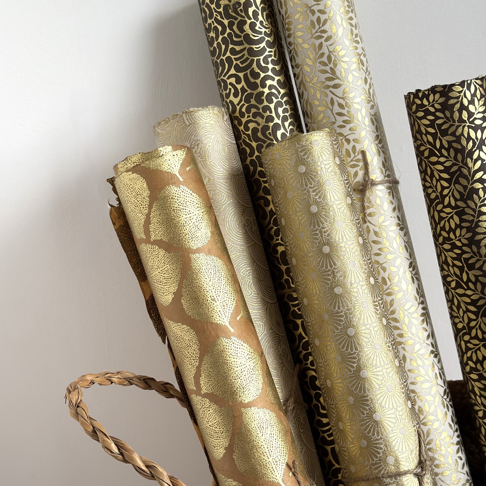 Nepalese handmade decorative lokta paper sheet with a gold metallic leaf pattern screen printed on a tan lokta paper.  Pictured rolled with other gold designs