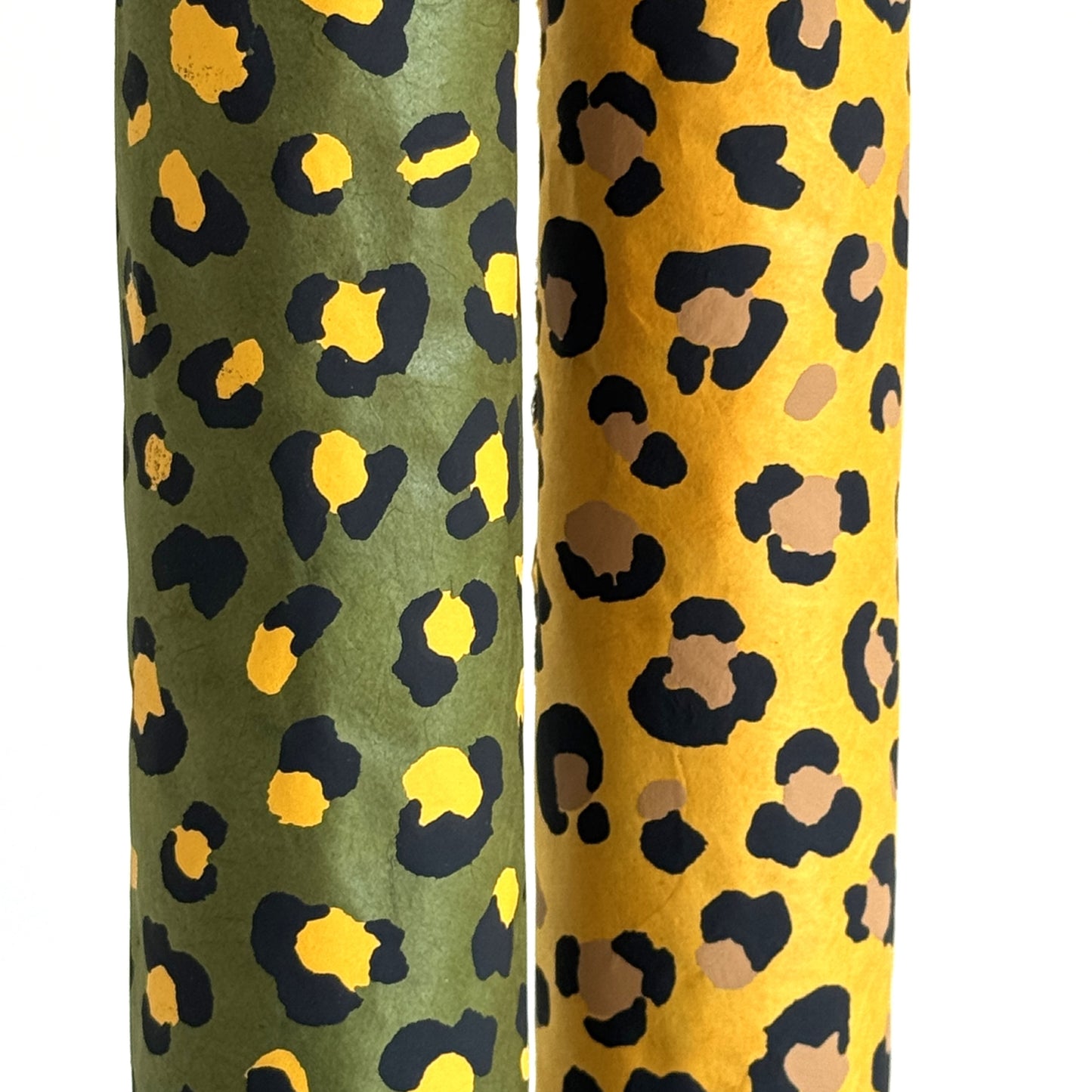 Nepalese handmade decorative lokta paper sheet with an animal print design in two colours, yellow and black, screen printed on a green lokta paper. Rolled and pictured with a version in yellow