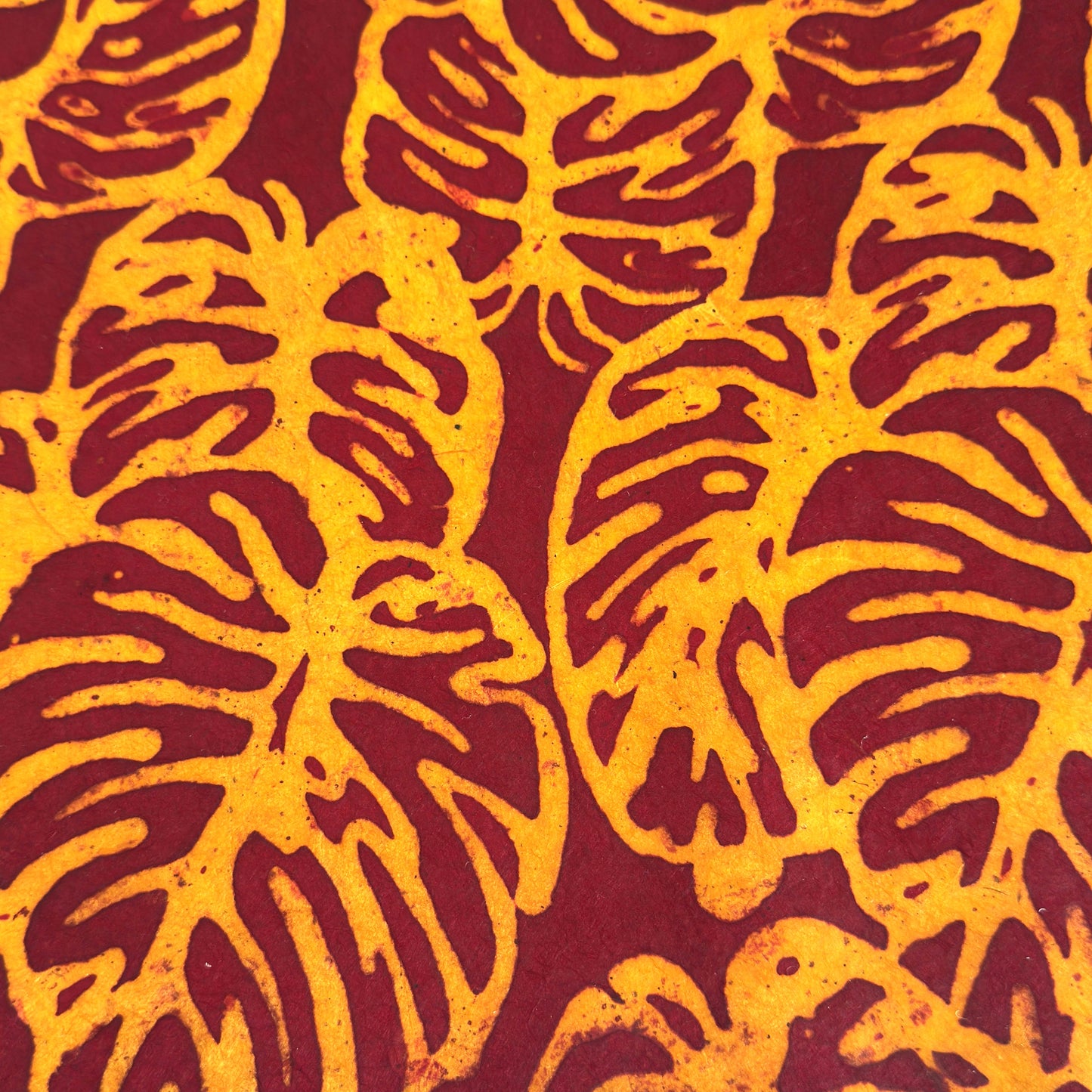 Nepalese handmade decorative lokta paper sheet with a leaf pattern in burgundy red and yellow.  Batik dyed using carved wooden blocks.